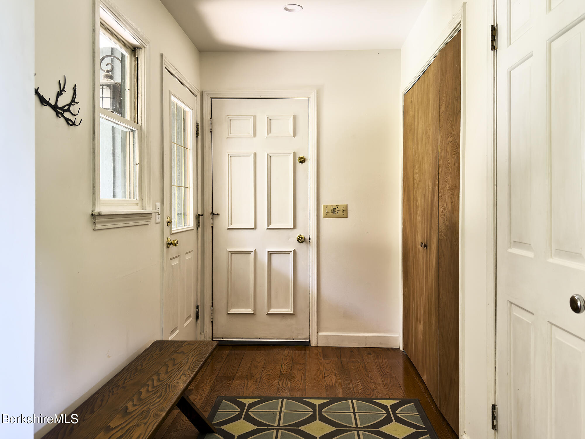 Entryway with a paneled front door, hardwood floor, long wooden bench, and tall wood-paneled closet.