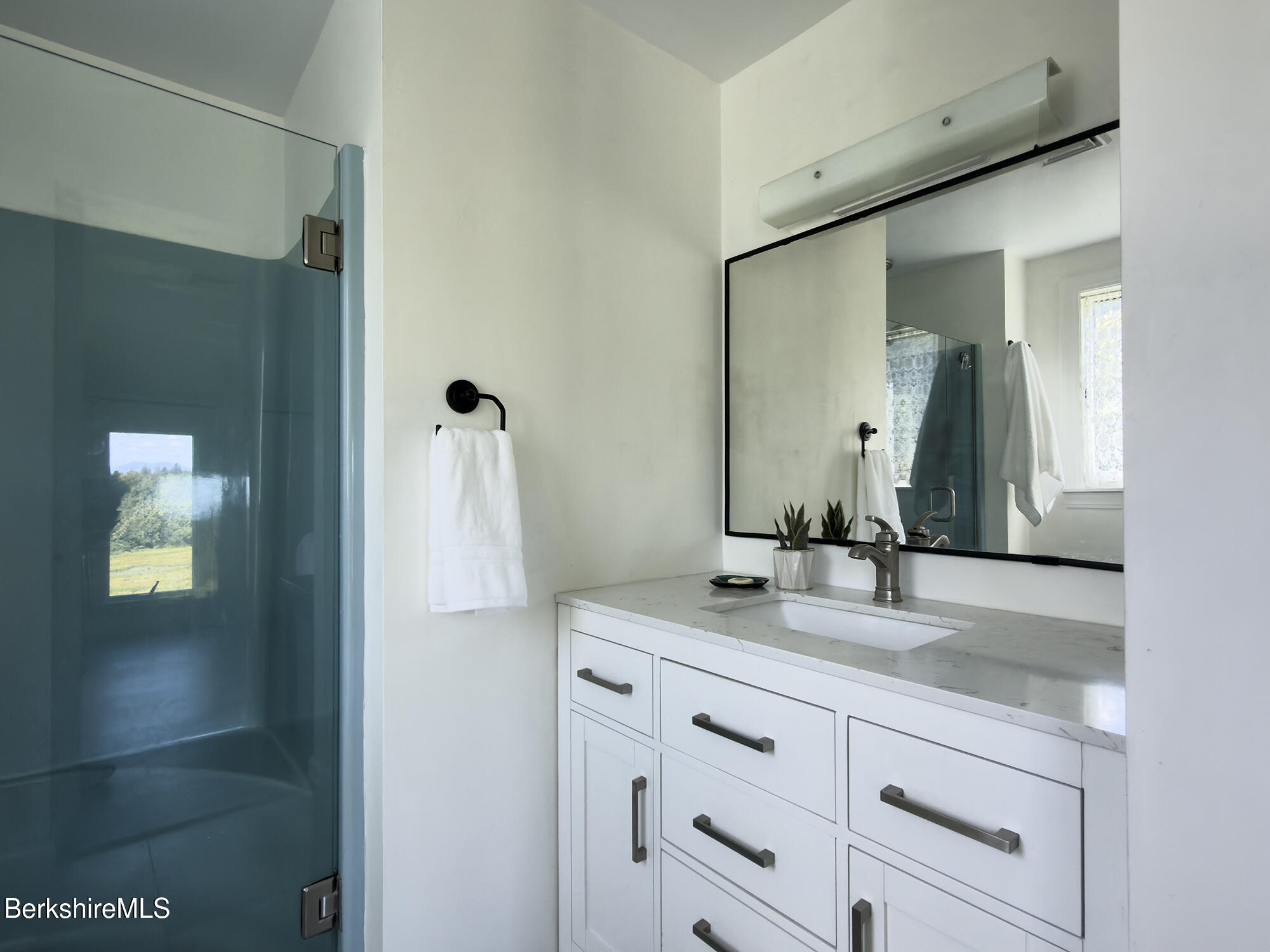 Modern bathroom with a blue-tinted glass shower and white vanity beneath a large mirror.