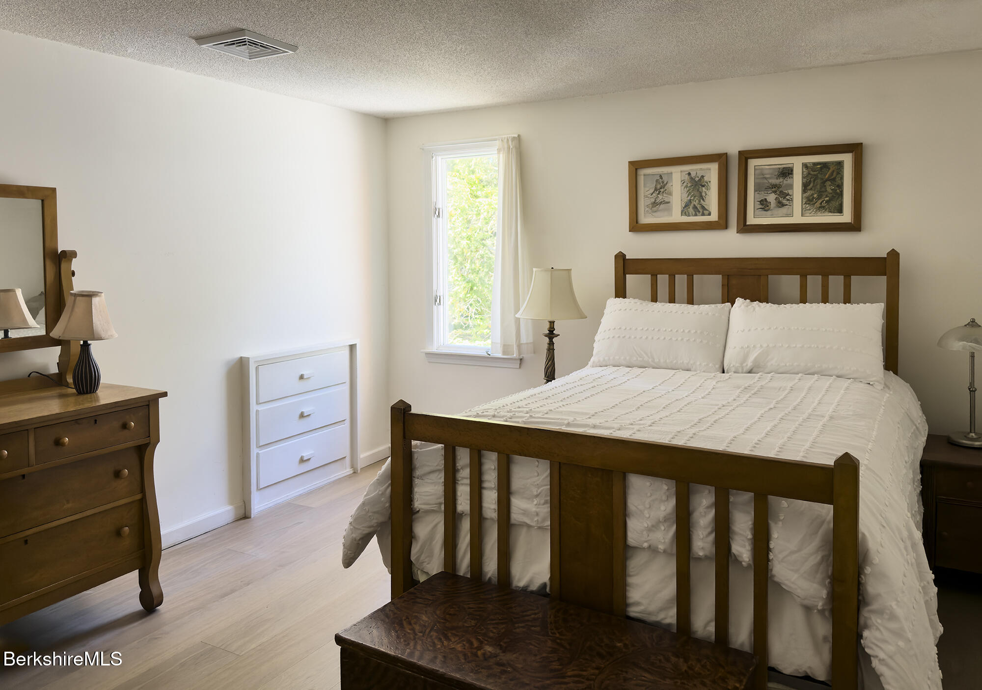 Bedroom with a dark wood bed, white bedding, matching dresser, and a window overlooking greenery.
