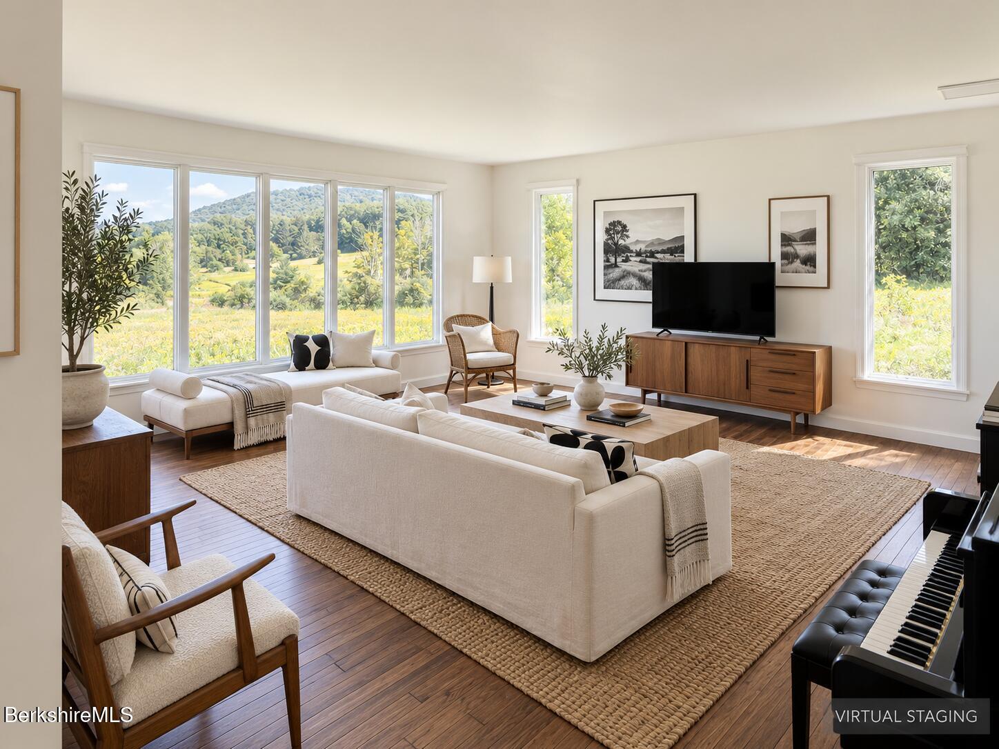Living room with light sofas, a piano, and large windows overlooking a green valley.