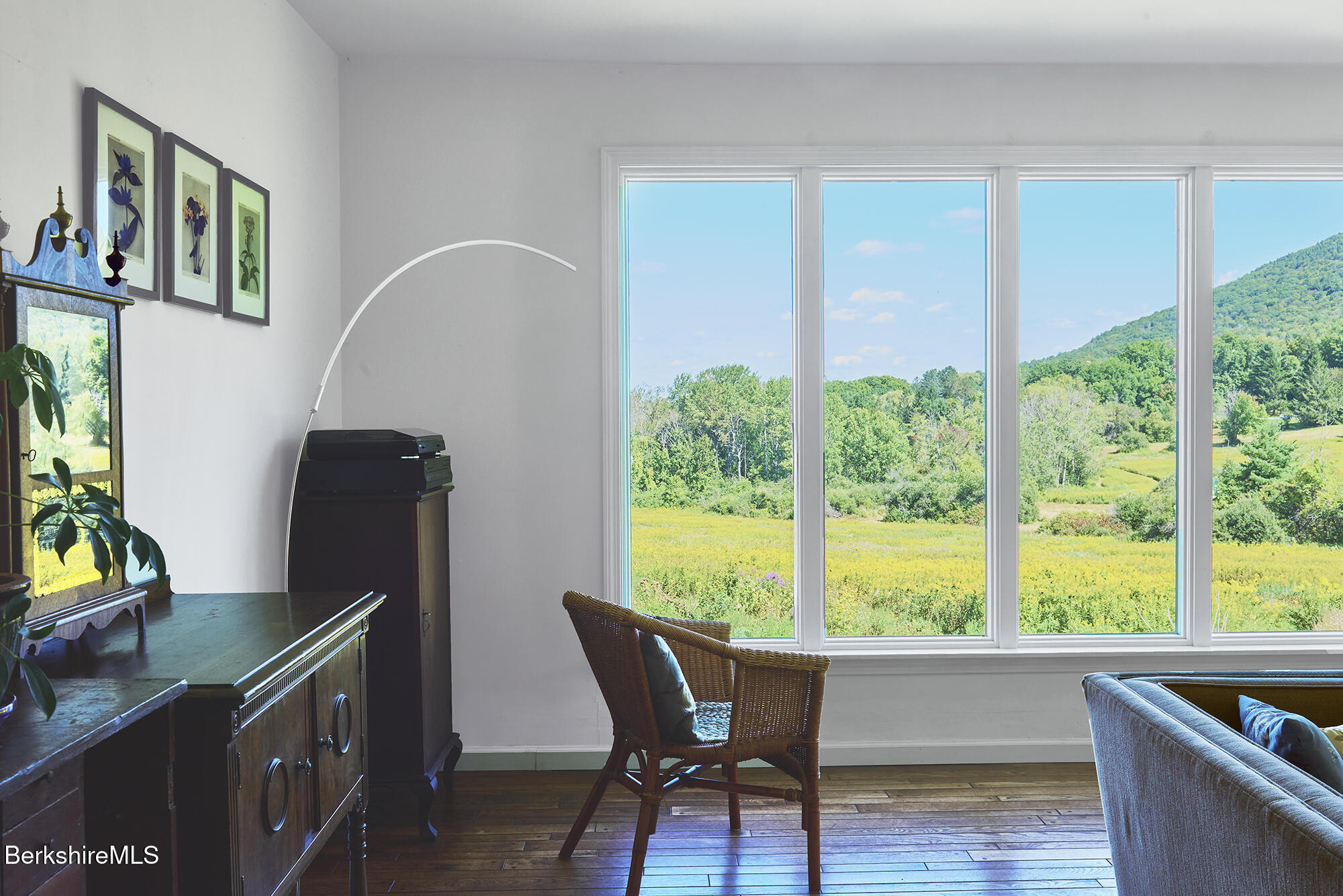 Living room with large windows overlooking a green meadow and wooded hills.