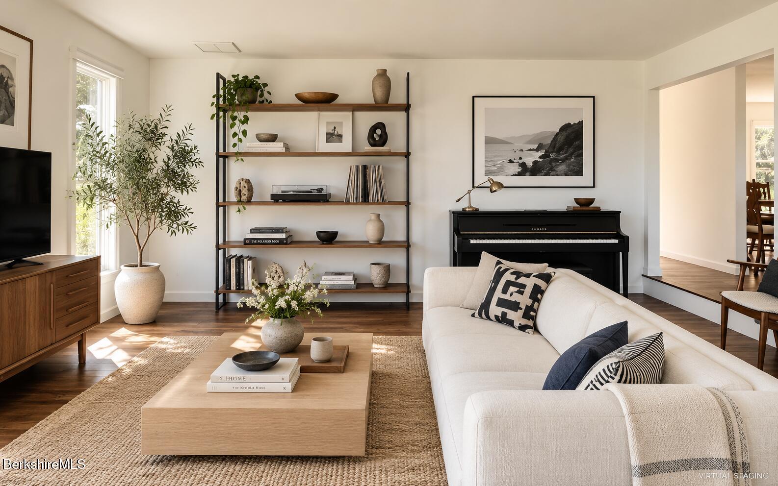 Virtually staged living room with a white sectional, black piano, open shelving, and hardwood floors.