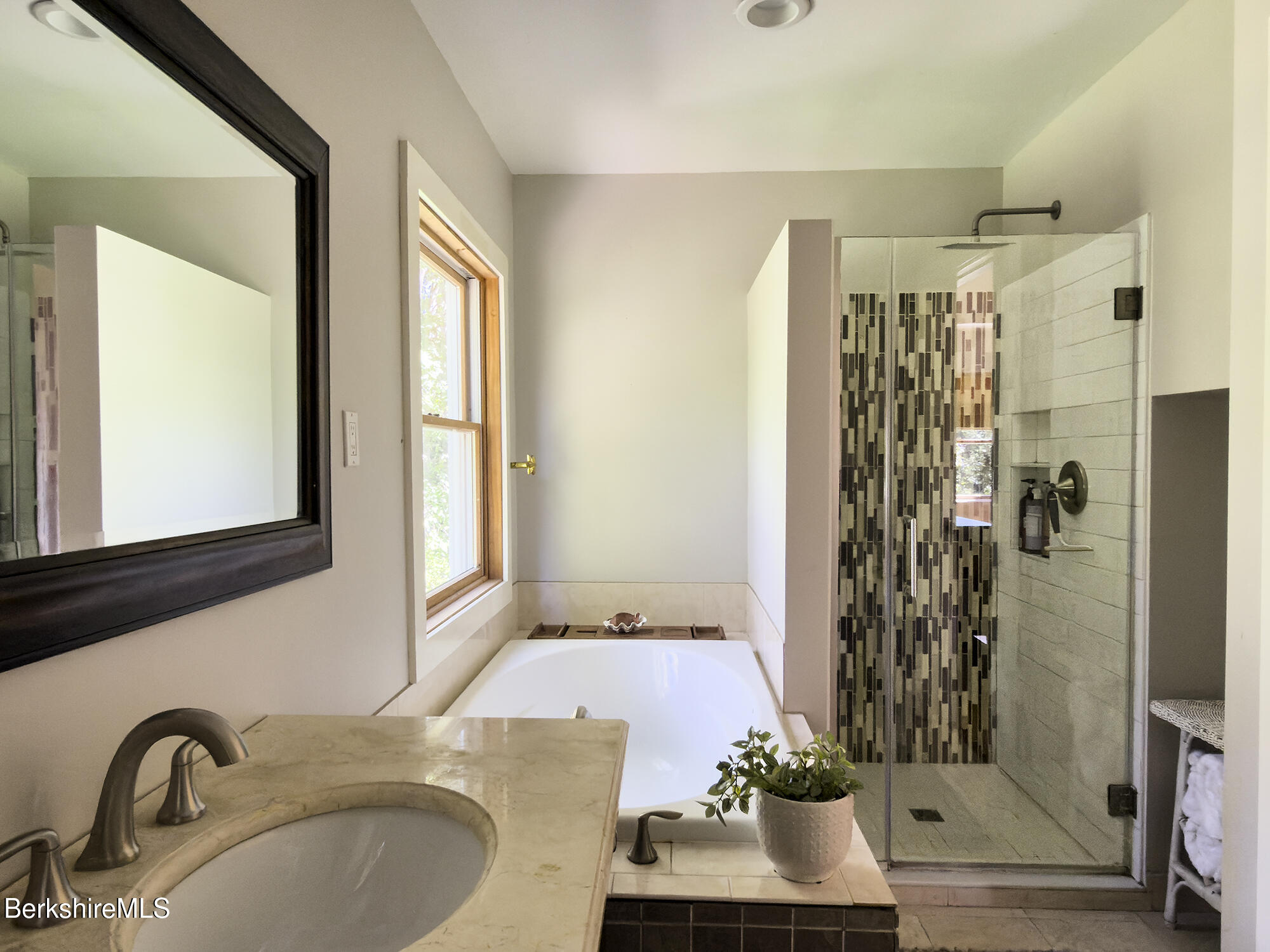 Bathroom with a soaking tub beneath a window and a glass shower with patterned mosaic tile.