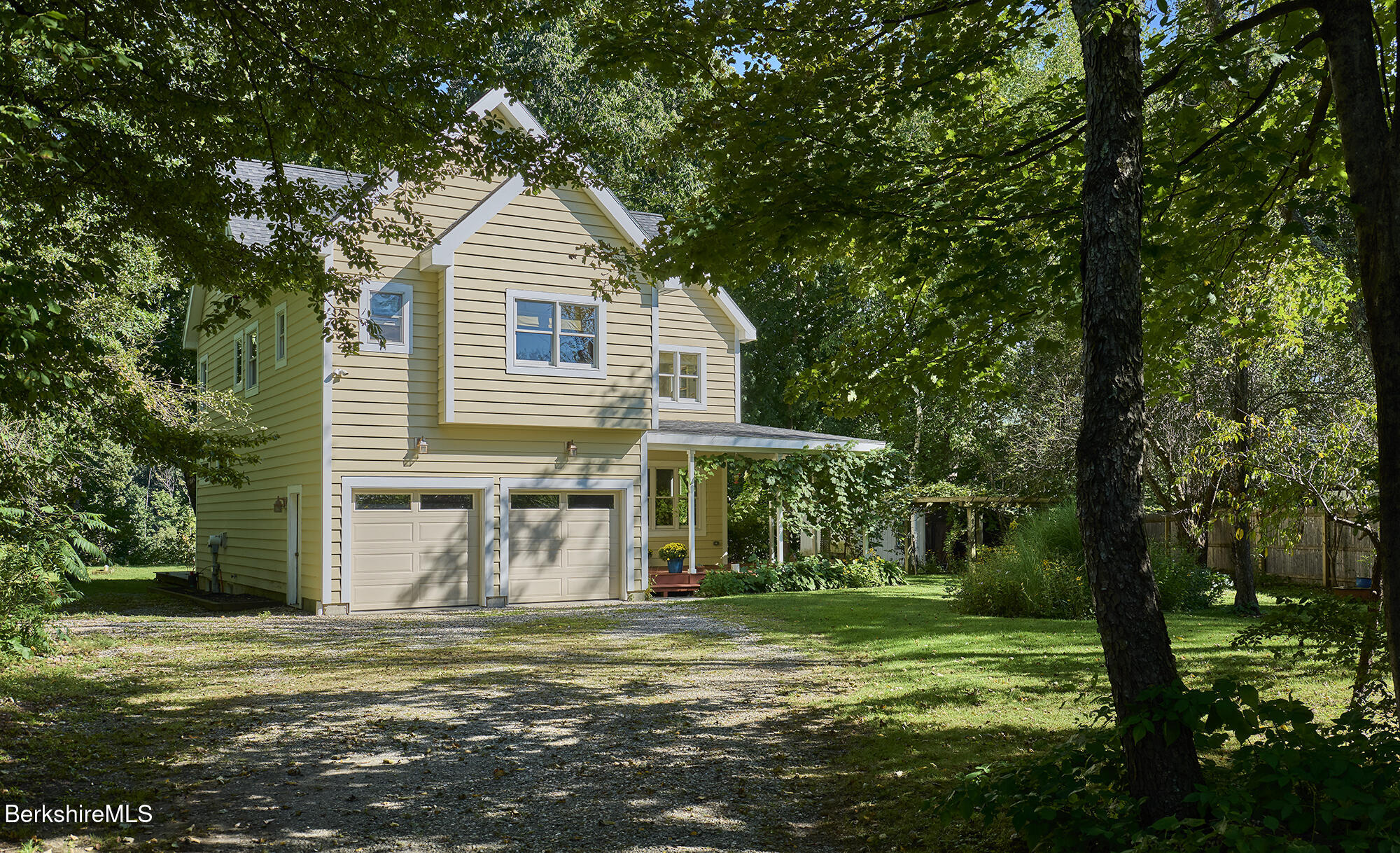 Pale yellow two-story house with a two-car garage, shaded by mature trees.