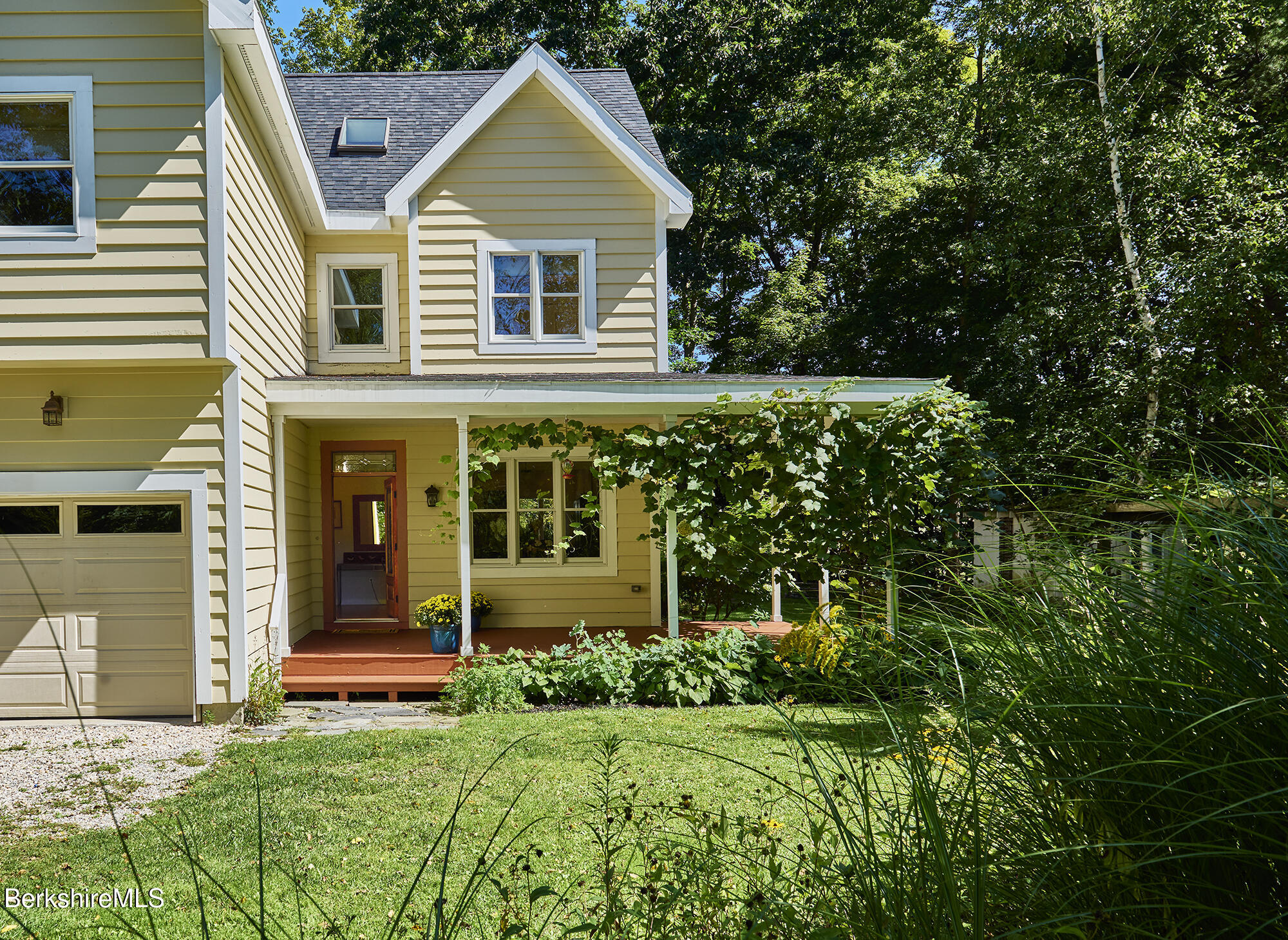 Yellow two-story house with a vine-covered porch, attached garage, and wooded surroundings.