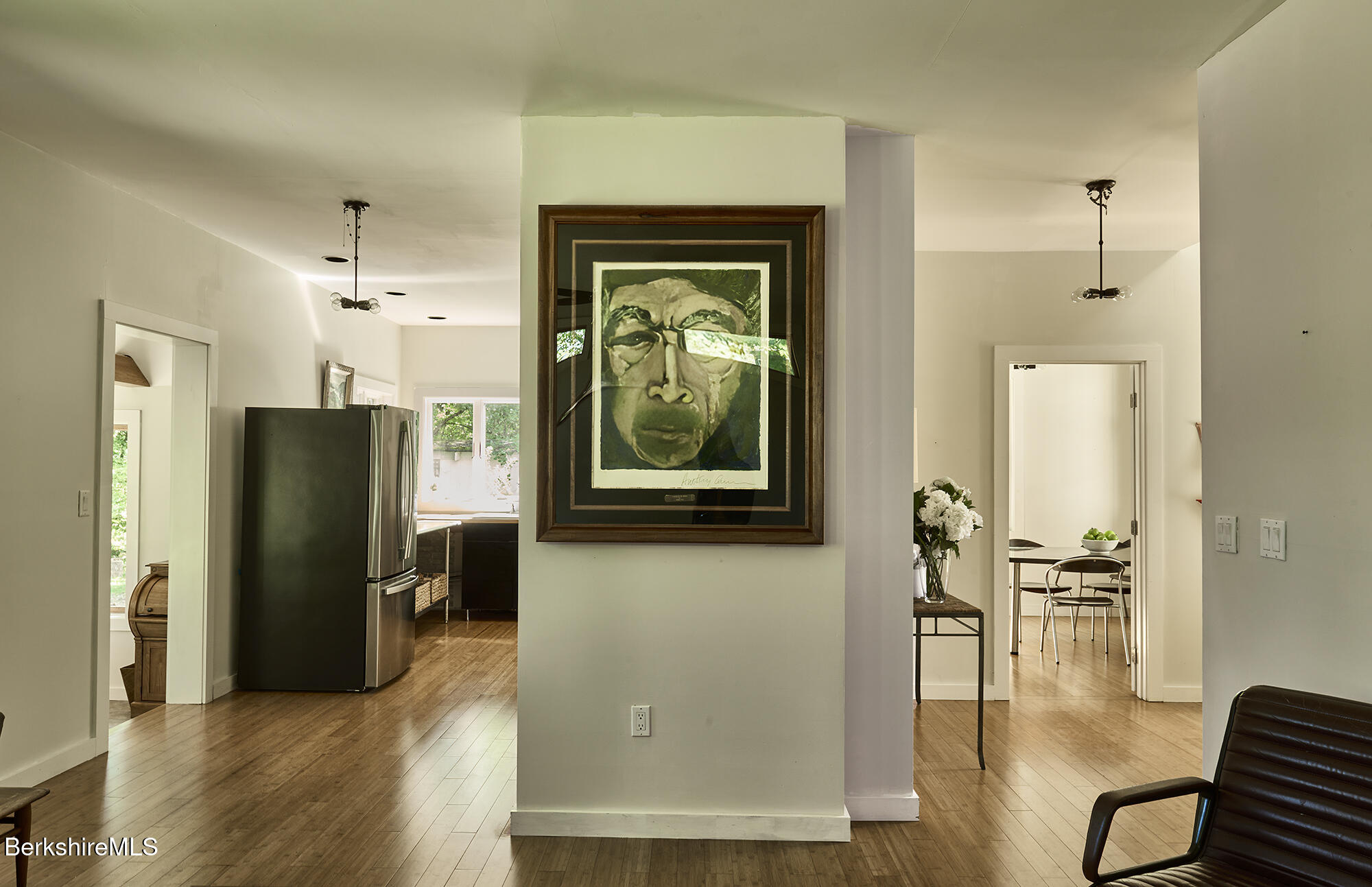 Home interior with wood floors, framed artwork, a stainless-steel refrigerator, and a dining area.