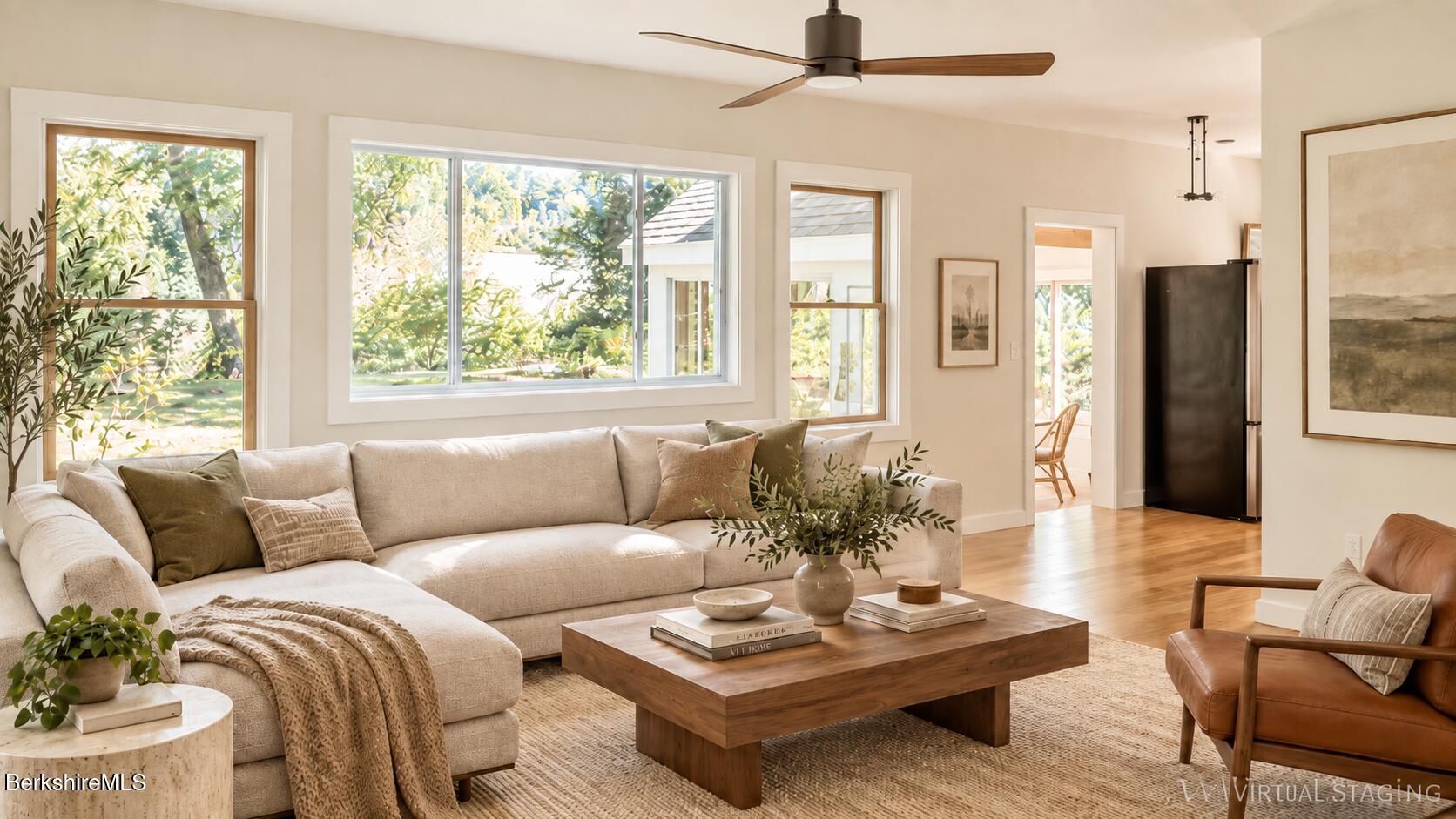 Living room with a cream sectional, wood coffee table, leather armchair, and large garden-facing windows.