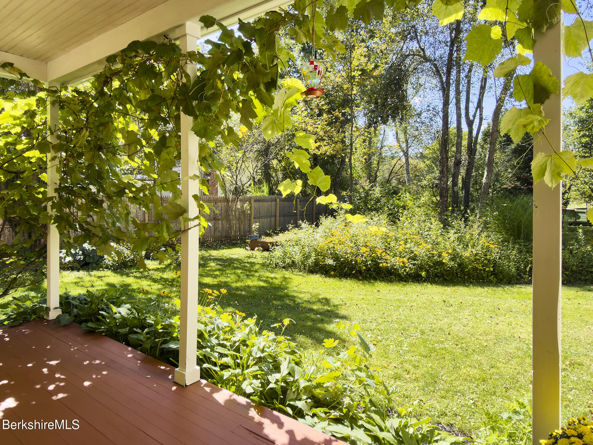 Covered porch overlooking a leafy garden, with grapevines around the posts and a hummingbird feeder.