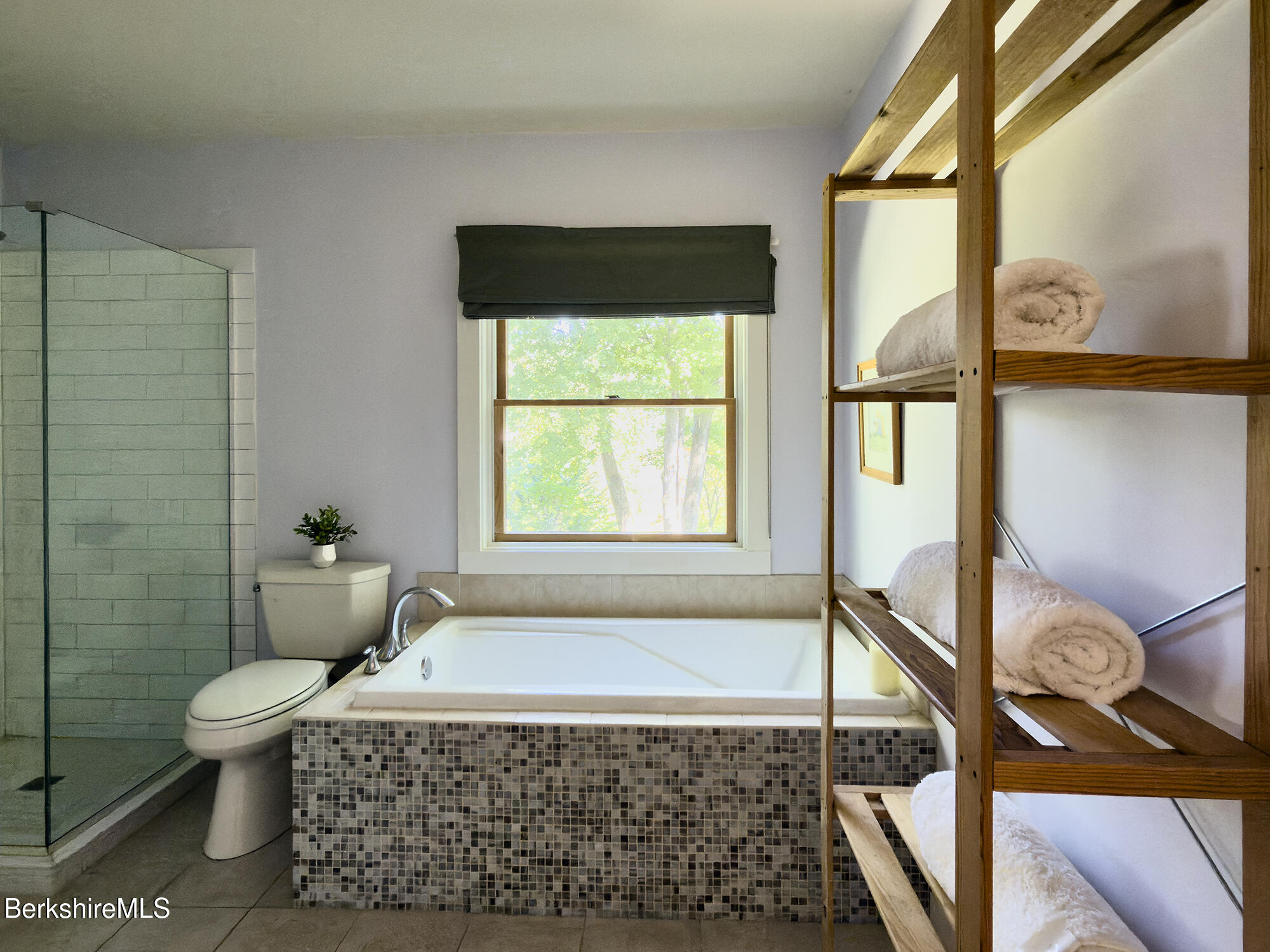 Bathroom with a tiled soaking tub, glass shower, and open wooden towel shelves.