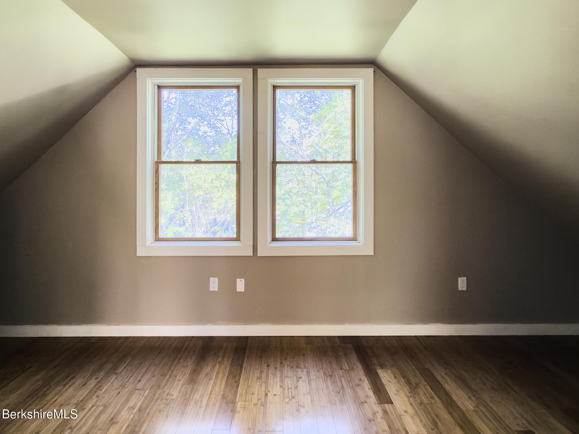 Empty room with a sloped ceiling, two windows, and hardwood floors.