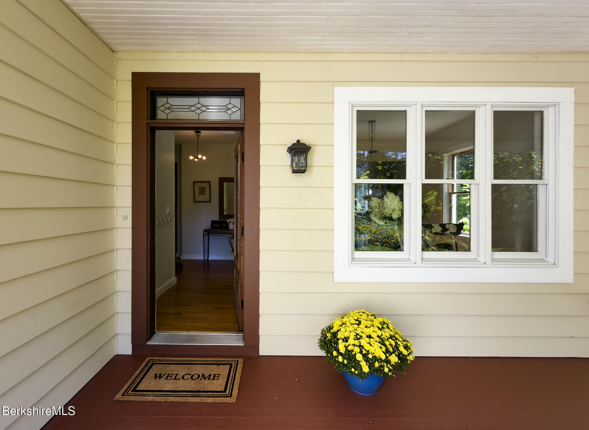 Home’s front entry with yellow siding, a white-trimmed window, and potted yellow flowers.