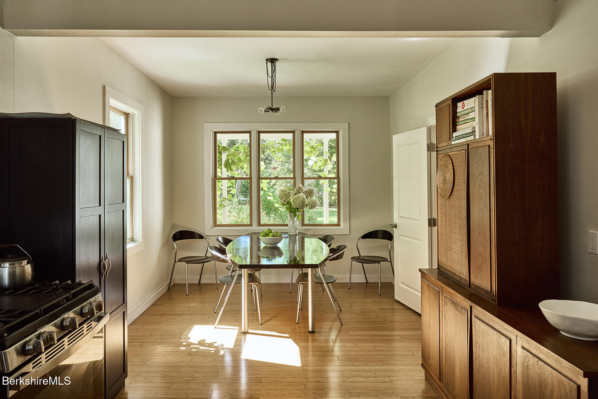 Dining area with a glass-topped table, wide garden-facing window, wood floors, and a tall wooden hutch.