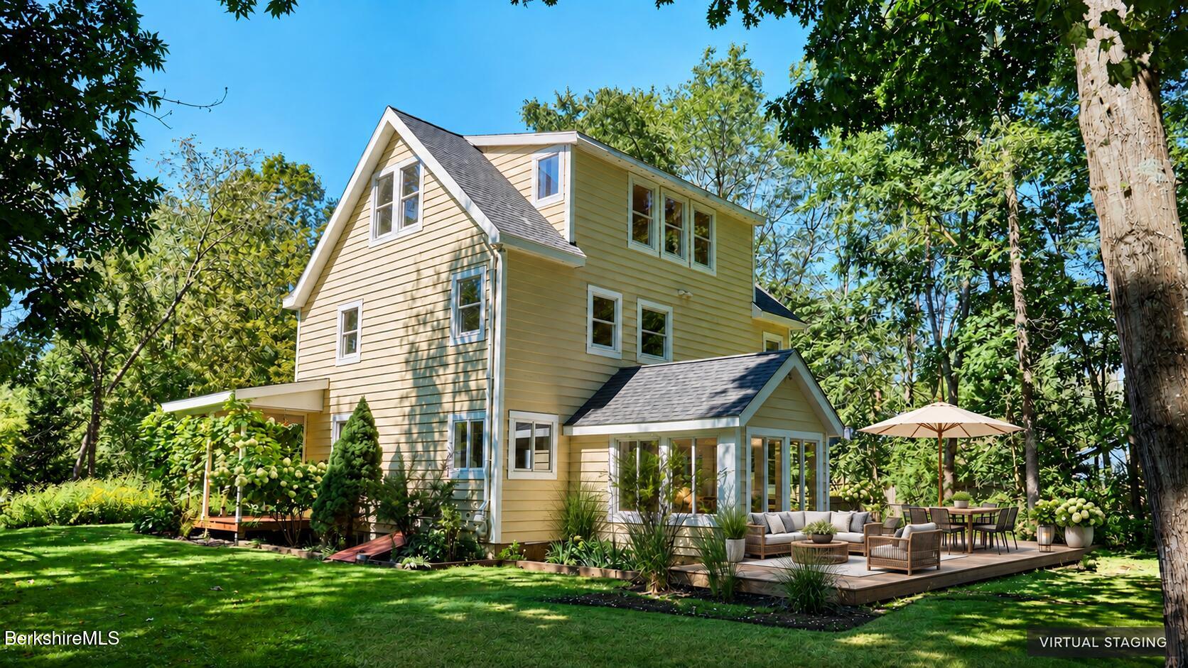 Pale yellow house with a furnished patio deck and umbrella, surrounded by mature trees.