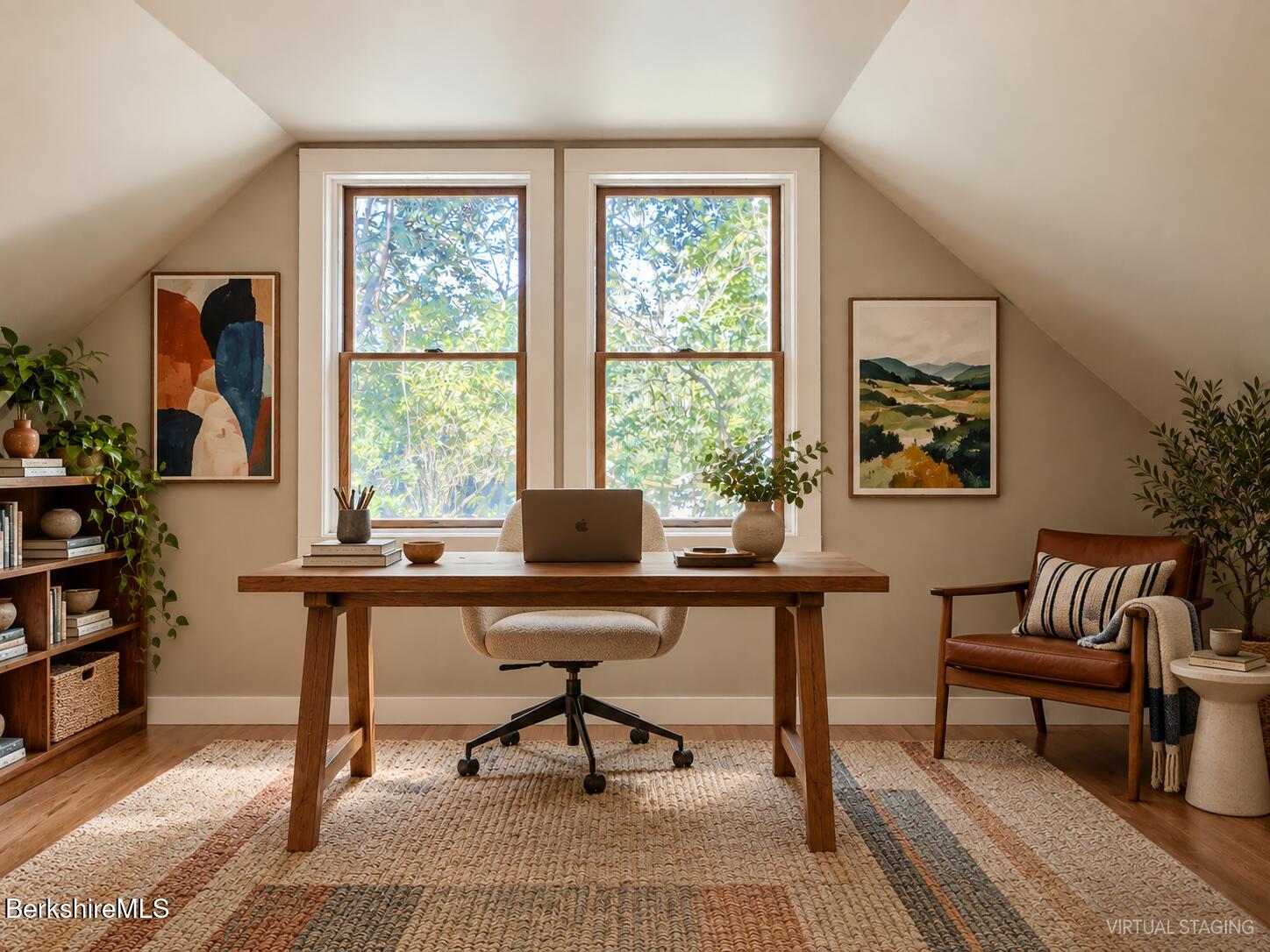 Attic home office with a wooden desk between two large windows and a leather reading chair.