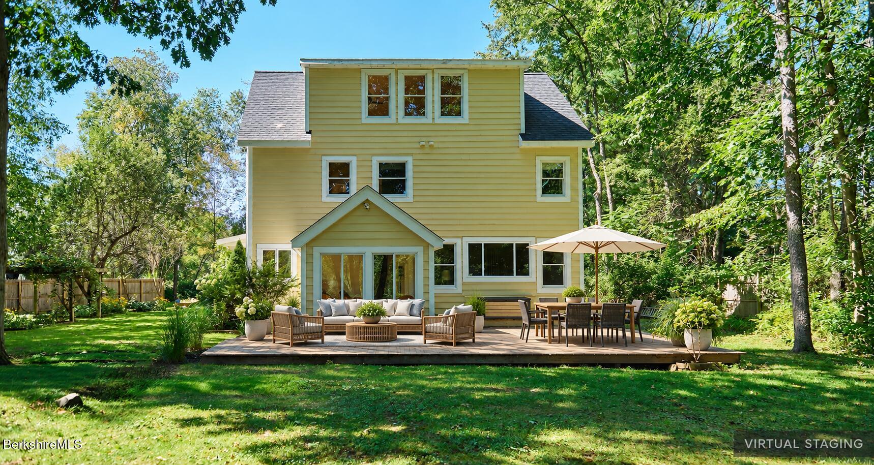 Yellow house with a staged backyard deck, lounge seating, and umbrella-shaded dining area.