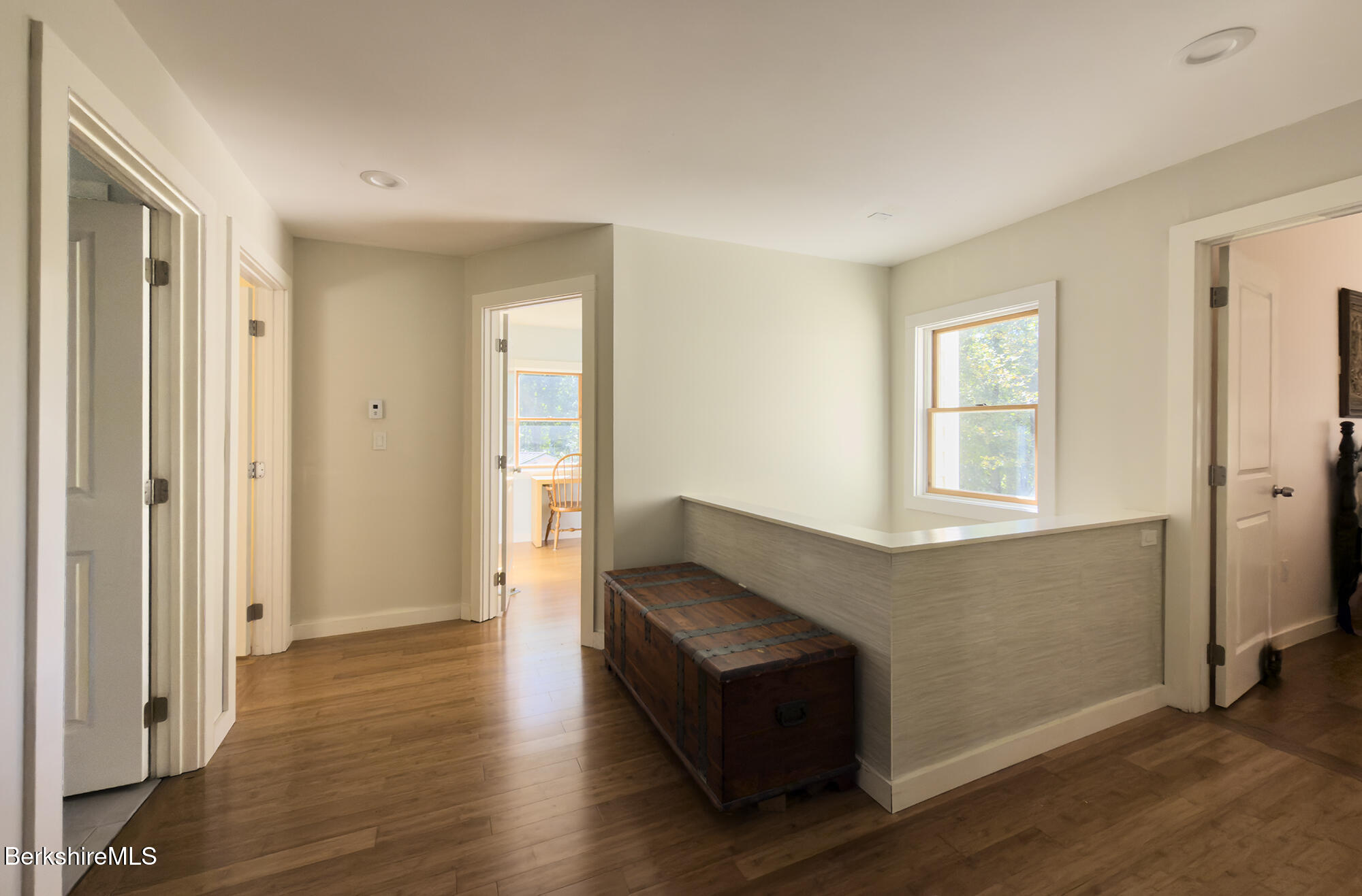Hallway with wood floors, a dark storage chest, and a half-height partition beneath a window.