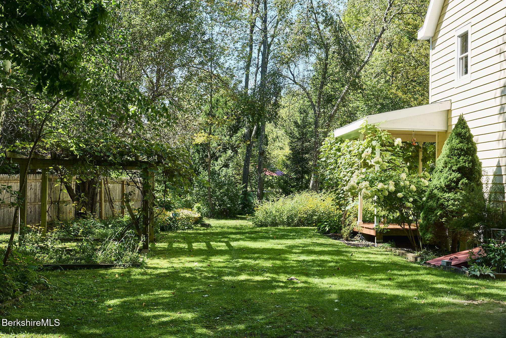 Landscaped backyard with a broad lawn, mature trees, garden beds, and a covered porch.
