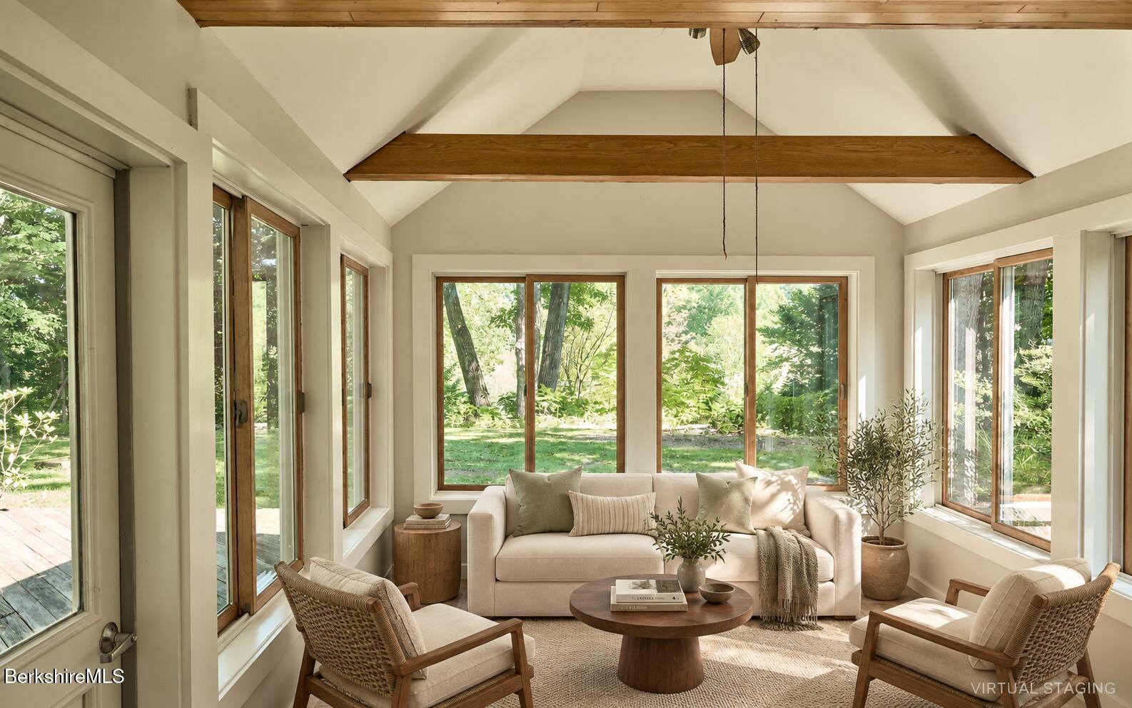 Sunroom with a cream sofa, woven lounge chairs, vaulted ceiling, and wide windows overlooking a garden.