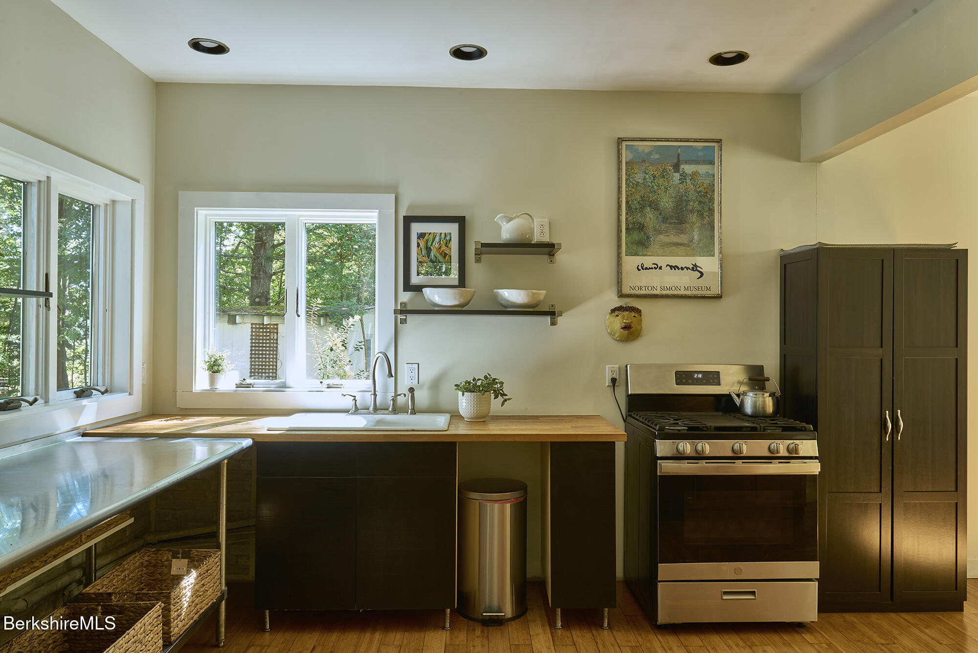 Kitchen with dark cabinetry, a stainless steel range, and a wood counter beneath large windows.