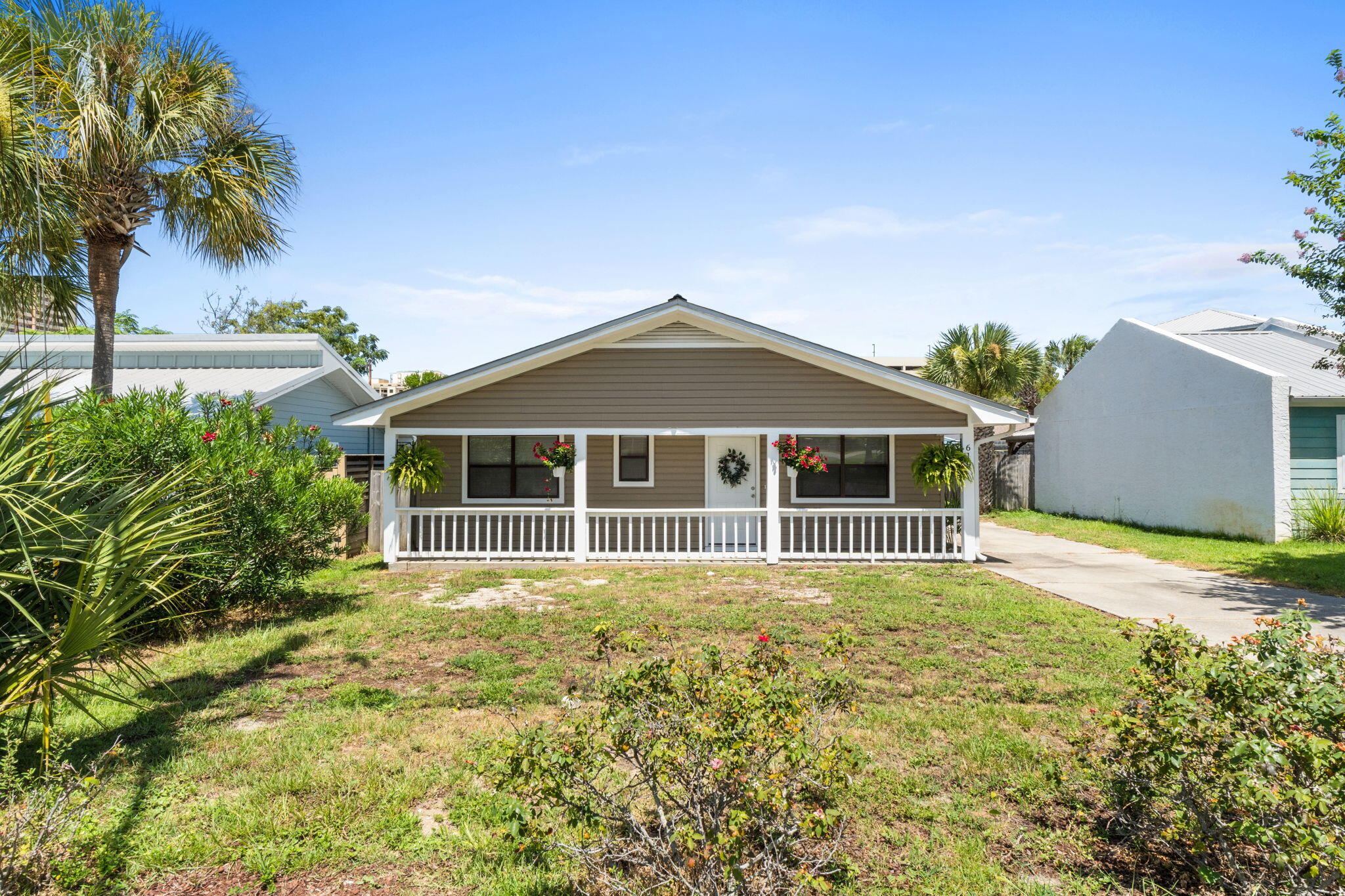 Taupe bungalow with a white-railed front porch, flower baskets, and palm trees.