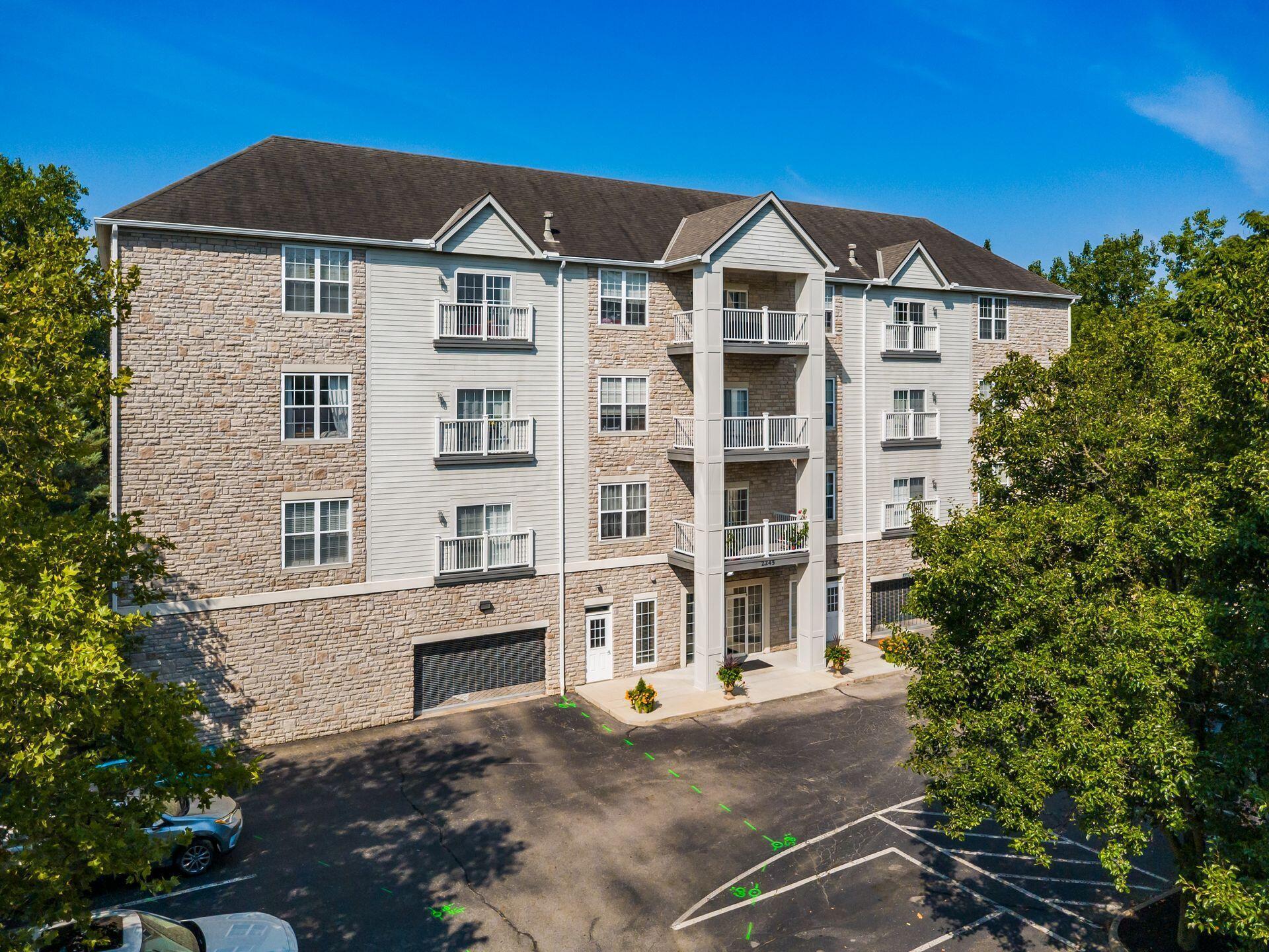 Multi-story apartment building with stone-and-siding exterior, stacked balconies, and parking in front.