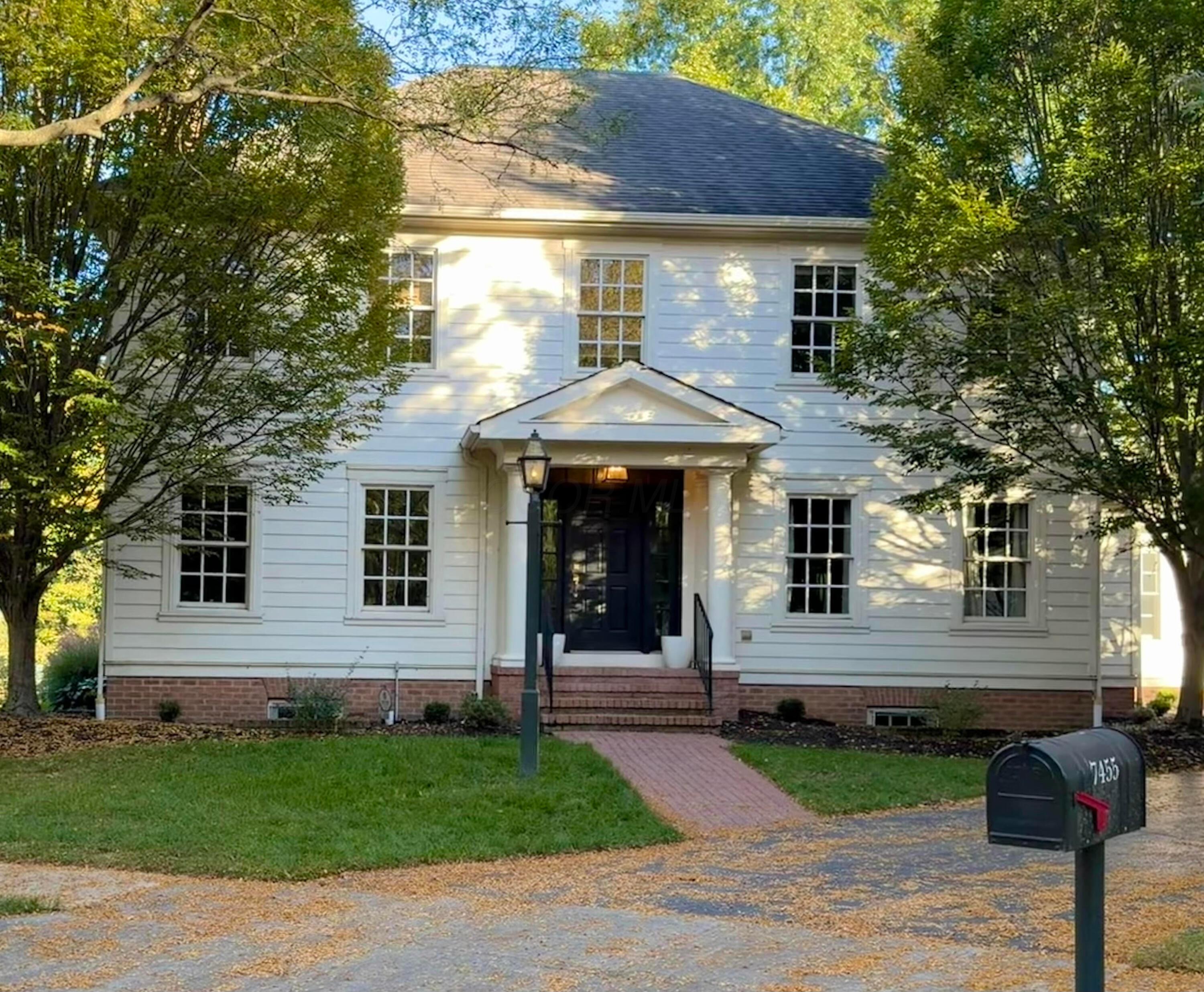 White two-story house with a dark front door, brick walkway, and mailbox marked 7455.