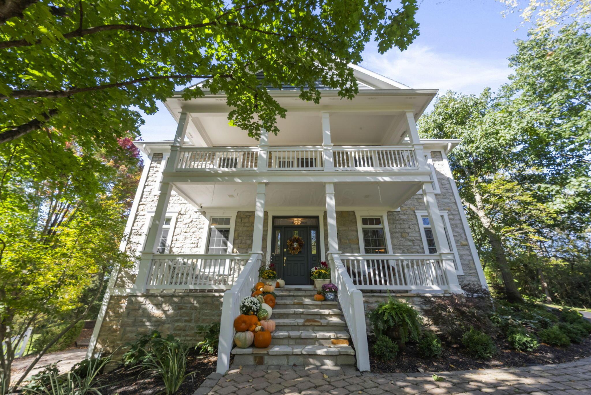 Stone-fronted home with a two-story white porch and pumpkin-decorated entry steps.