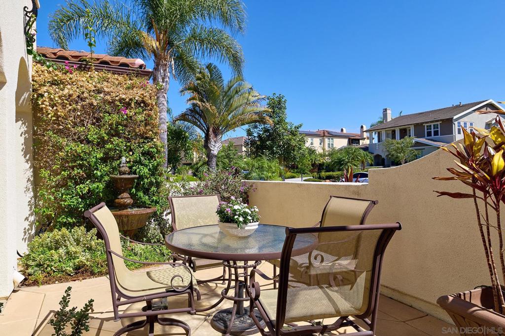 Outdoor patio with a glass dining table, mesh chairs, palms, and a small fountain.