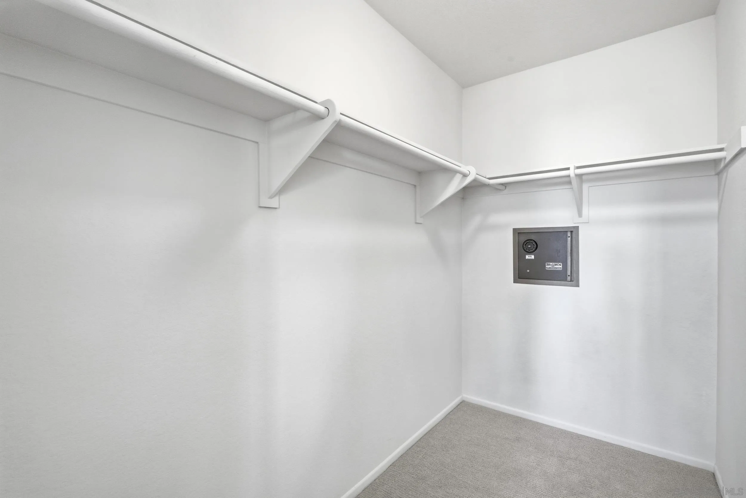 Walk-in closet with wraparound hanging rods, carpeted floor, and a wall-mounted safe.