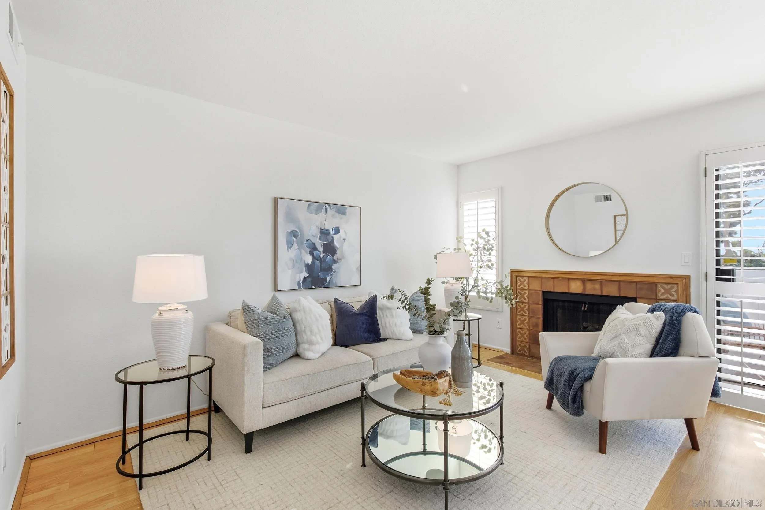 Furnished living room with a tiled fireplace, cream seating, and plantation shutters.