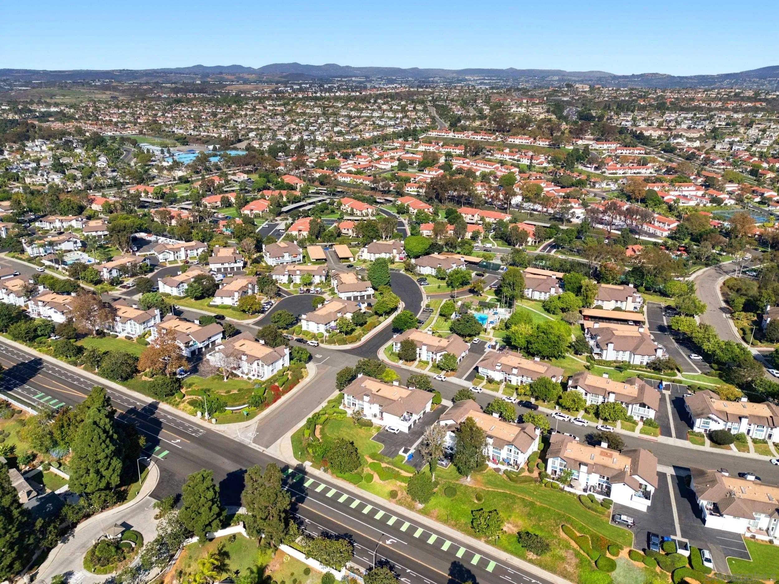Aerial view of a residential neighborhood with curving streets, tiled roofs, and swimming pools.