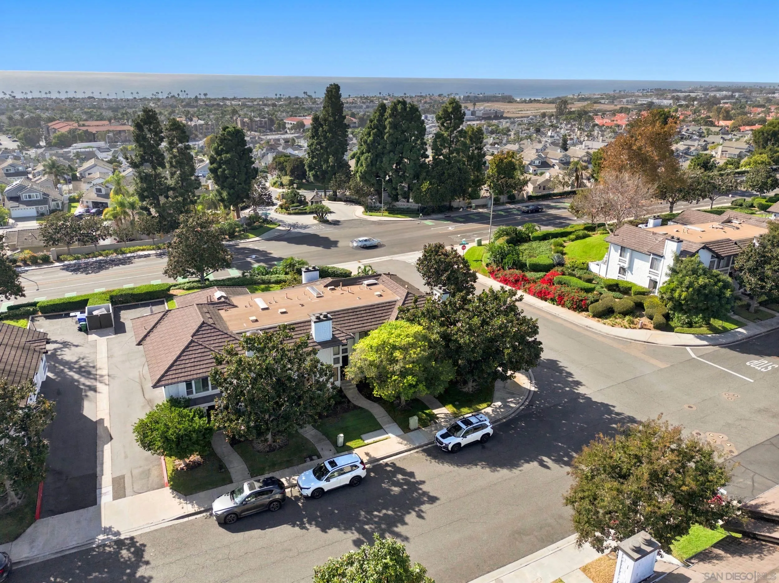 Aerial view of the corner home, with landscaped grounds, neighborhood streets, and the distant ocean.