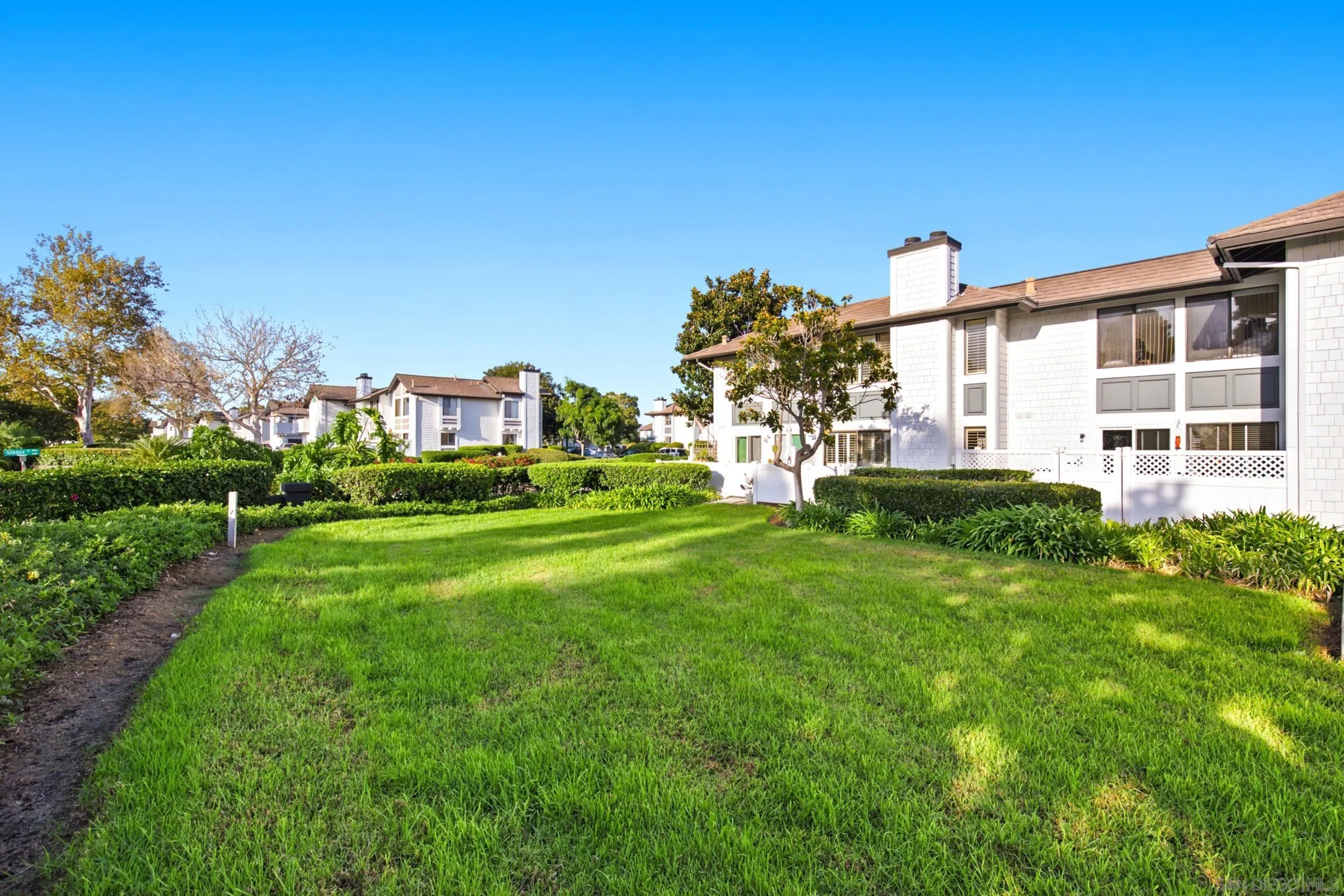 White multi-unit residential building beside a broad lawn, hedges, and landscaped grounds.
