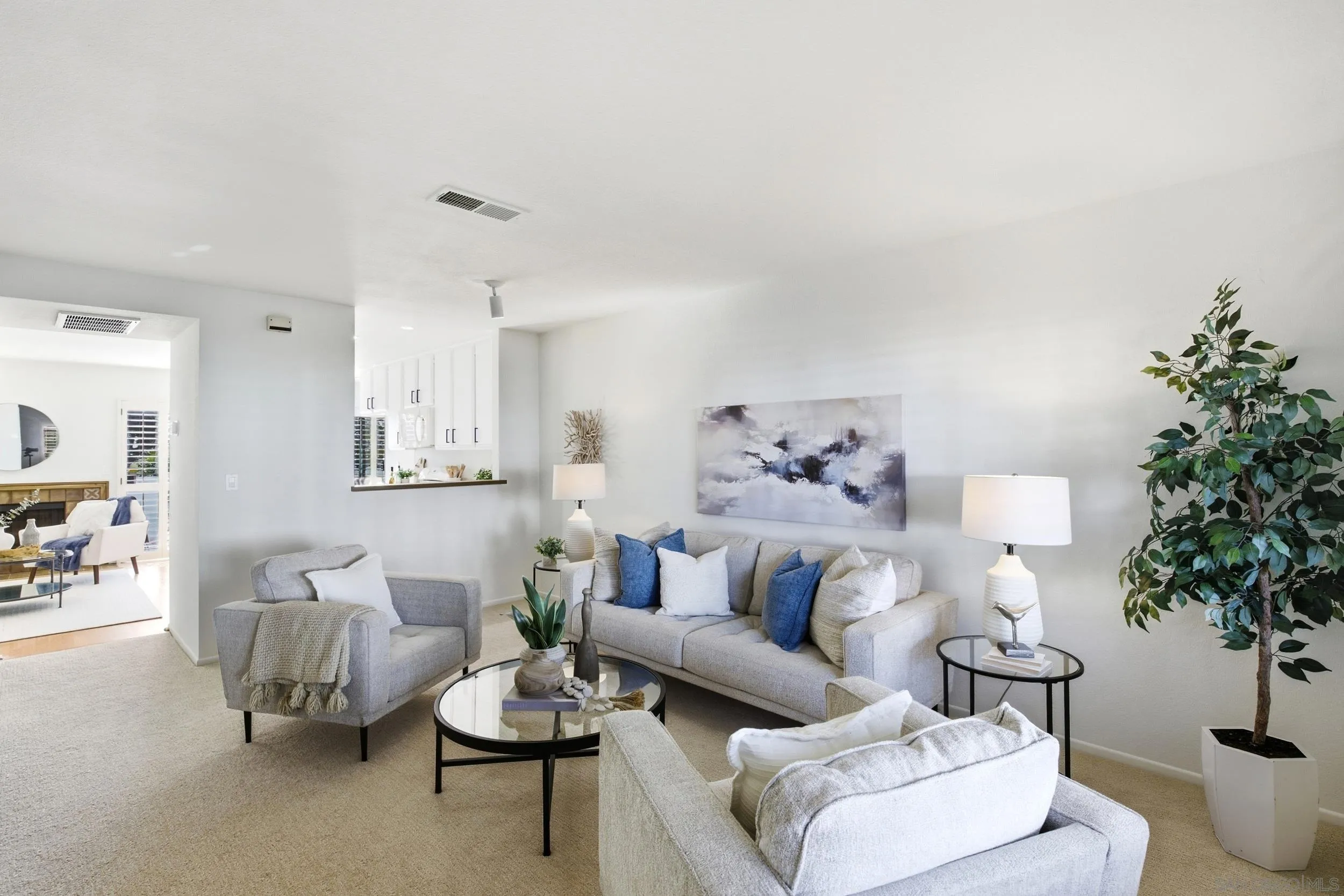 Living room with gray seating, blue accent pillows, abstract art, and a large potted tree.