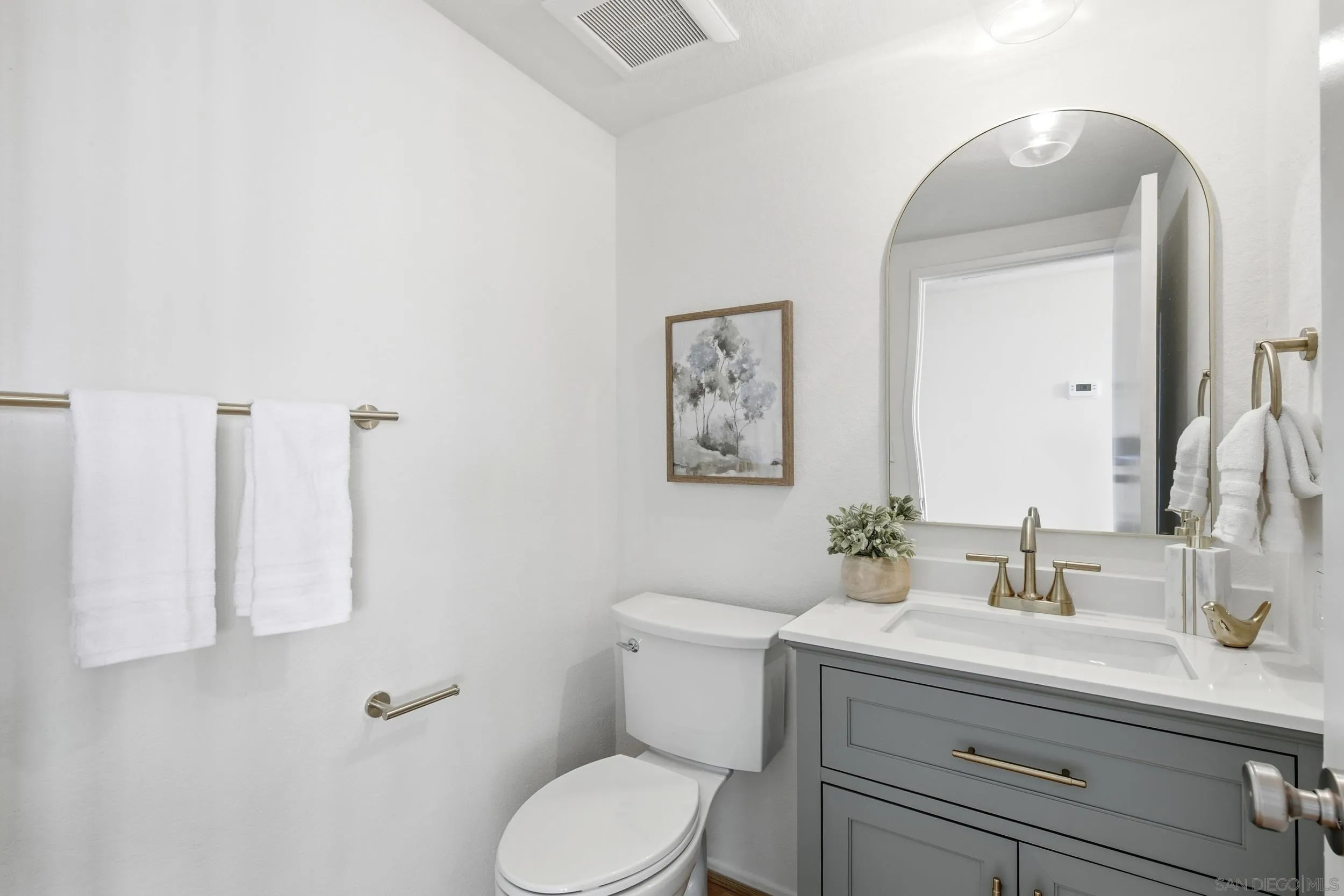 Bathroom with a gray vanity, arched mirror, brass fixtures, and white towels.