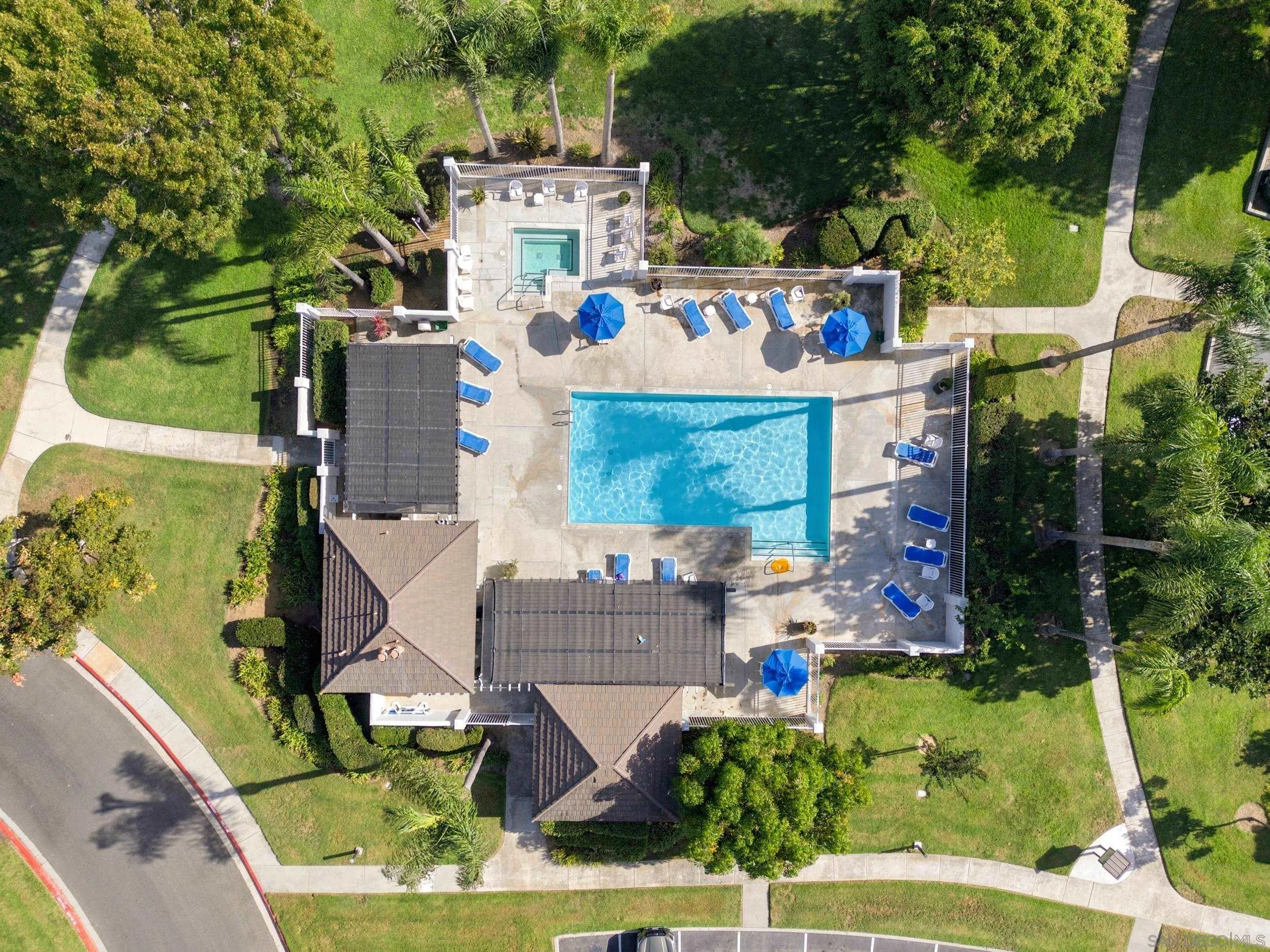 Aerial view of a rectangular pool with blue umbrellas, lounge chairs, and a small spa.