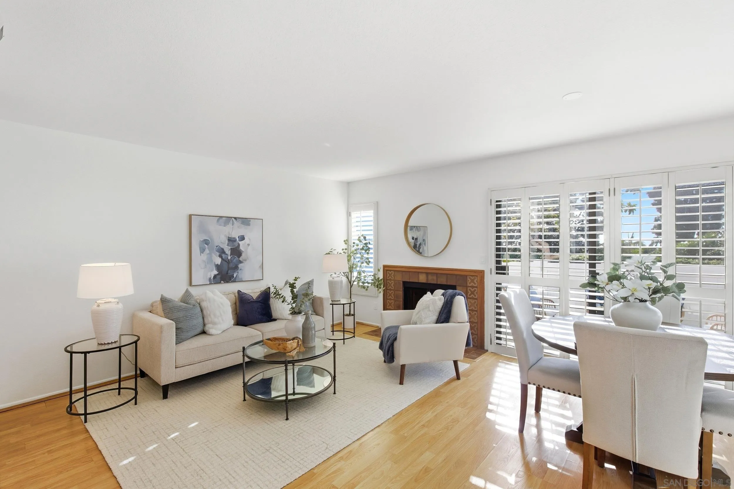 Bright living and dining room with a tiled fireplace, beige sofa, and plantation shutters.