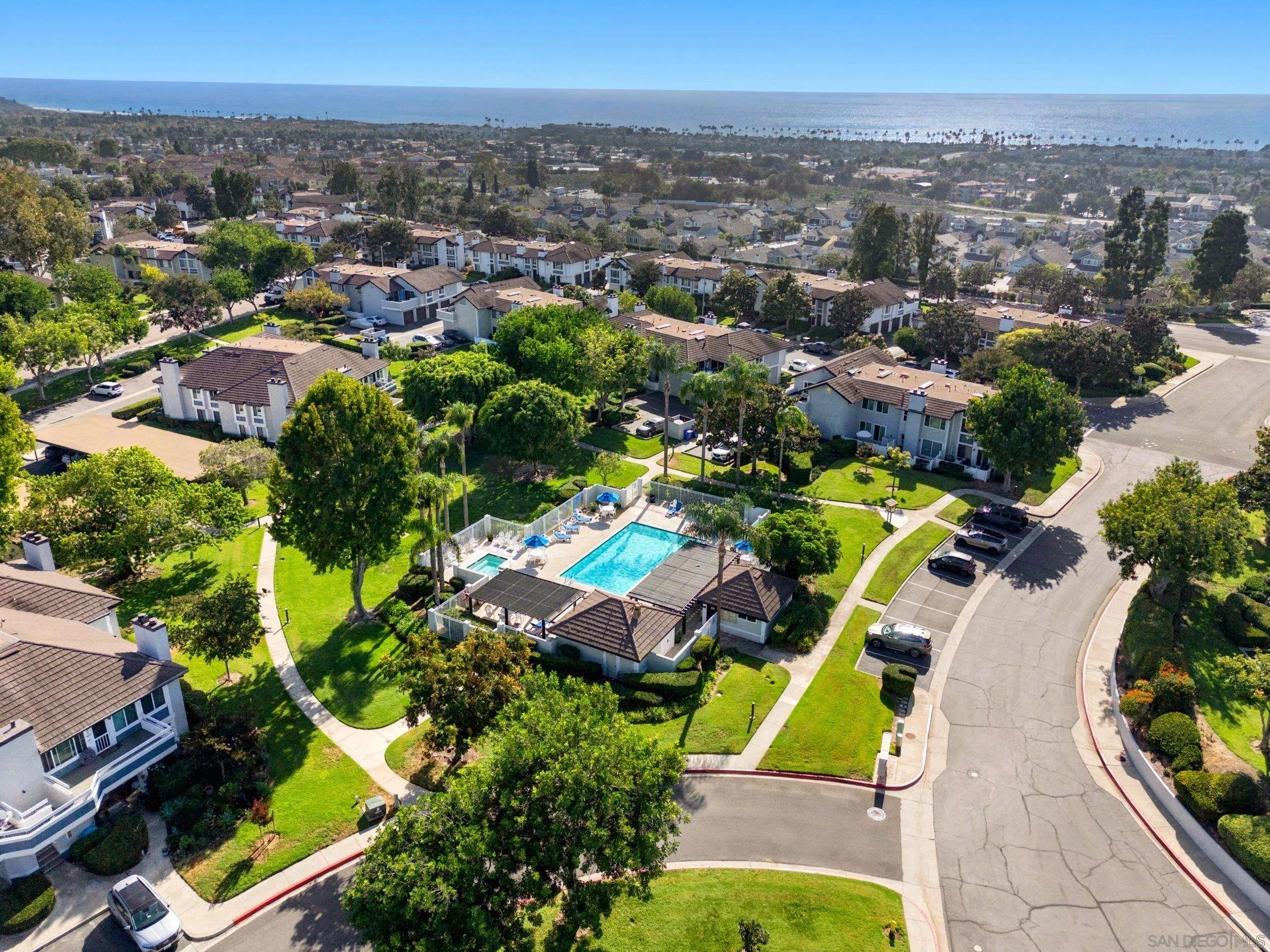 Aerial view of homes and a community pool with the ocean on the horizon.