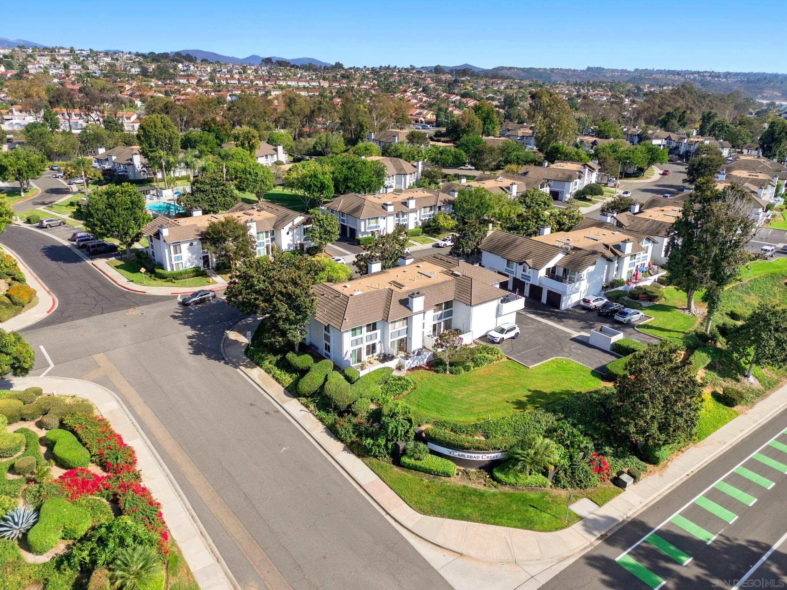 Aerial view of Carlsbad Crest, with landscaped buildings, a swimming pool, and distant hills.