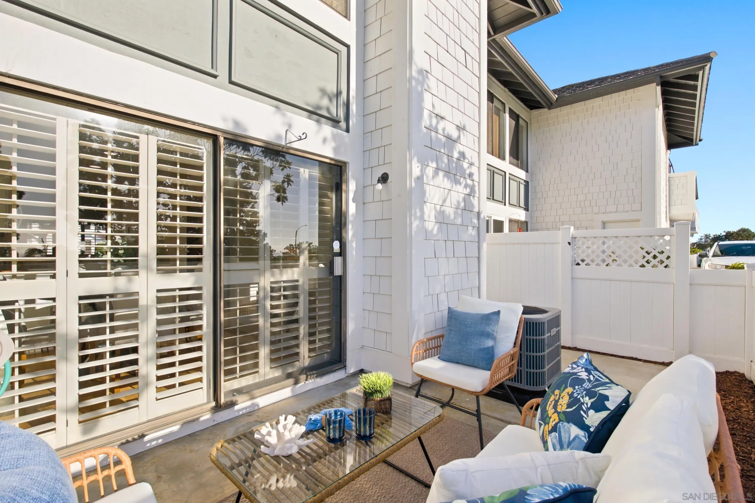 Furnished patio with white seating, glass coffee table, shuttered doors, and privacy fencing.