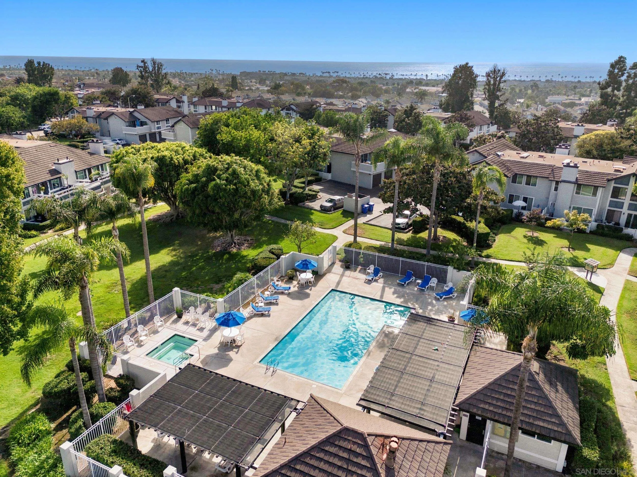 Aerial view of a community pool and surrounding homes, with the ocean in the distance.