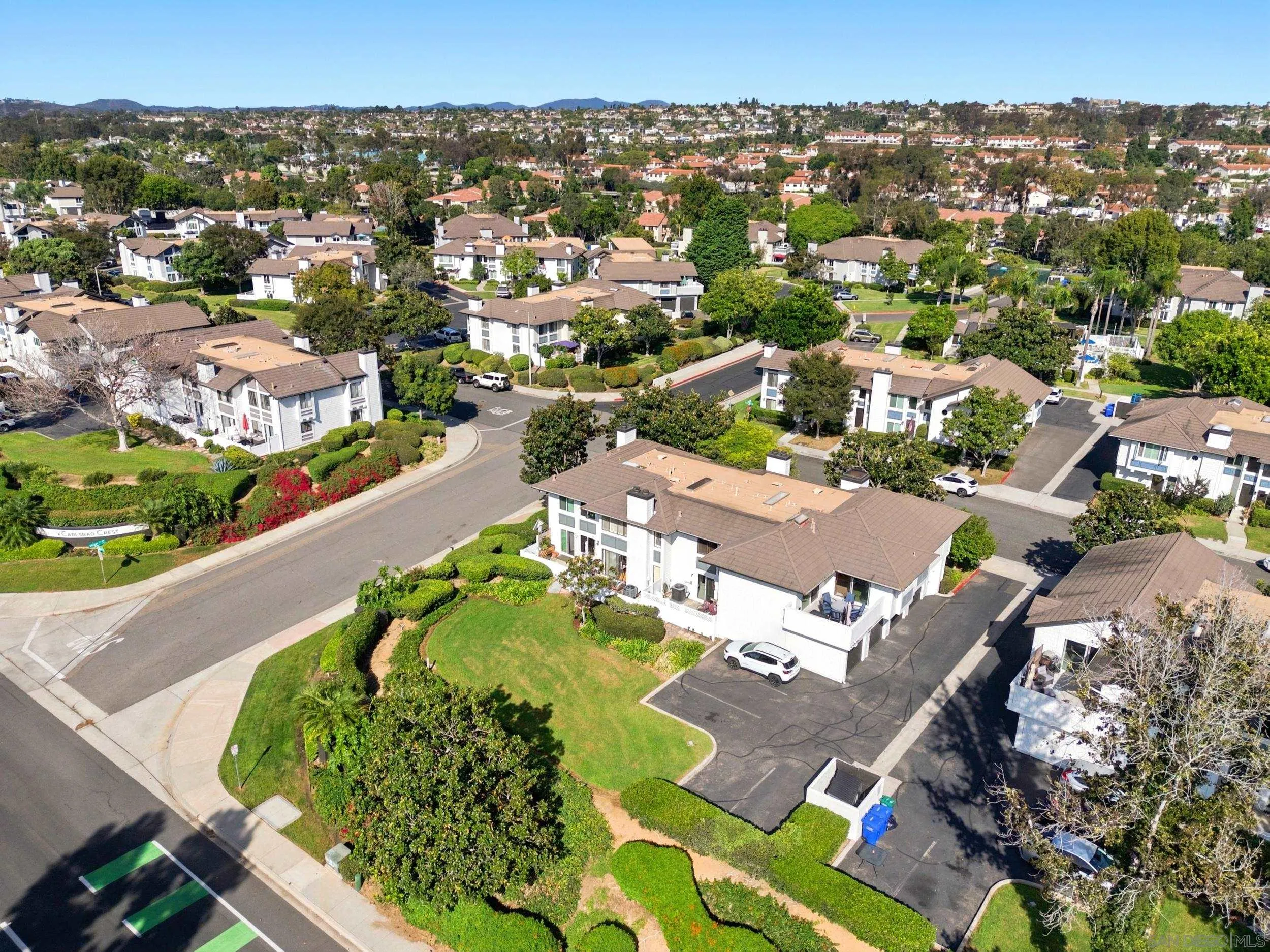 Aerial view of a landscaped Carlsbad neighborhood with white homes, curving streets, and distant hills.