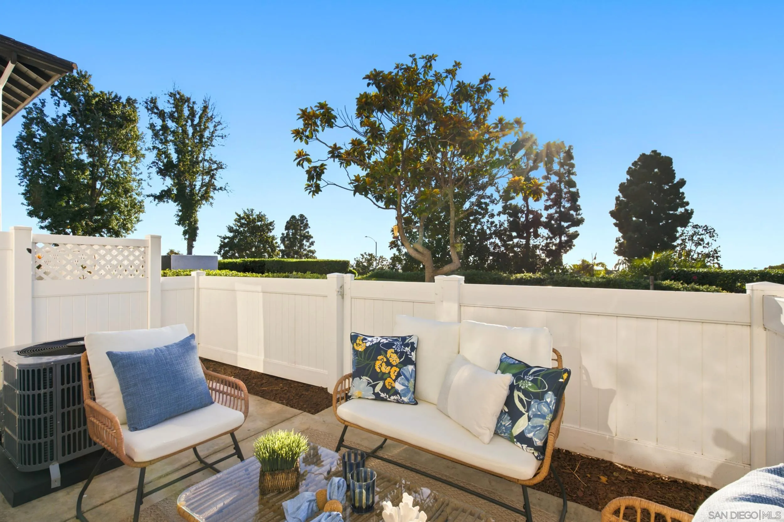 Furnished patio with wicker seating, patterned cushions, and a white privacy fence.