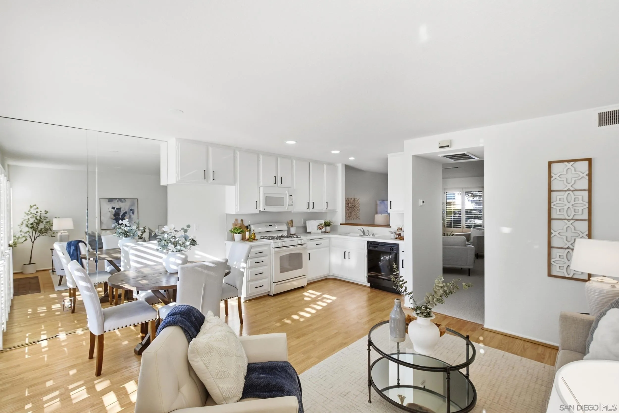 Open-plan kitchen and dining area with white cabinets, light wood floors, and a mirrored wall.