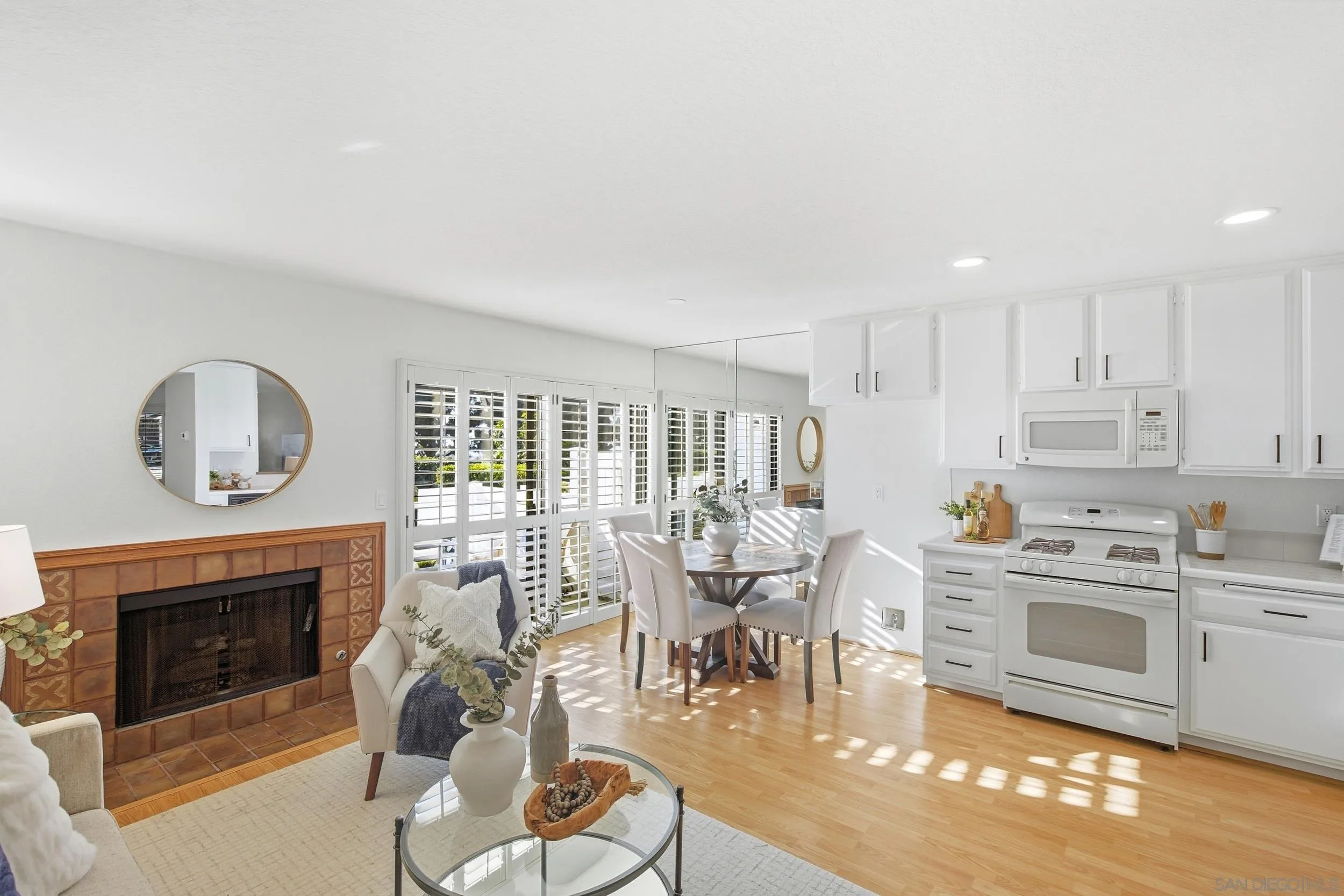 Open-plan living room with tiled fireplace, dining nook, and bright white kitchen.