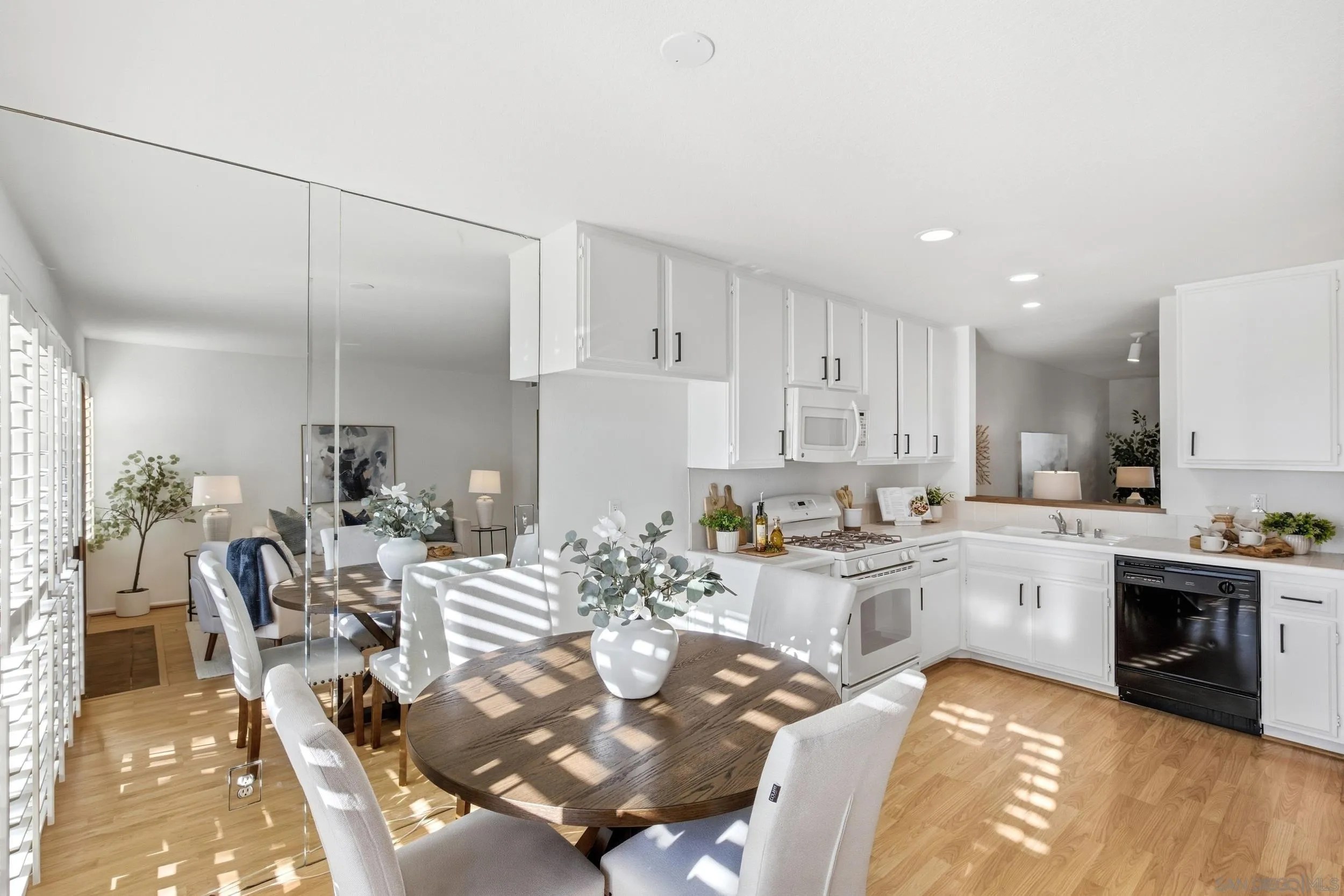 Bright kitchen and dining area with white cabinets, a round wood table, and sunlight through plantation shutters.