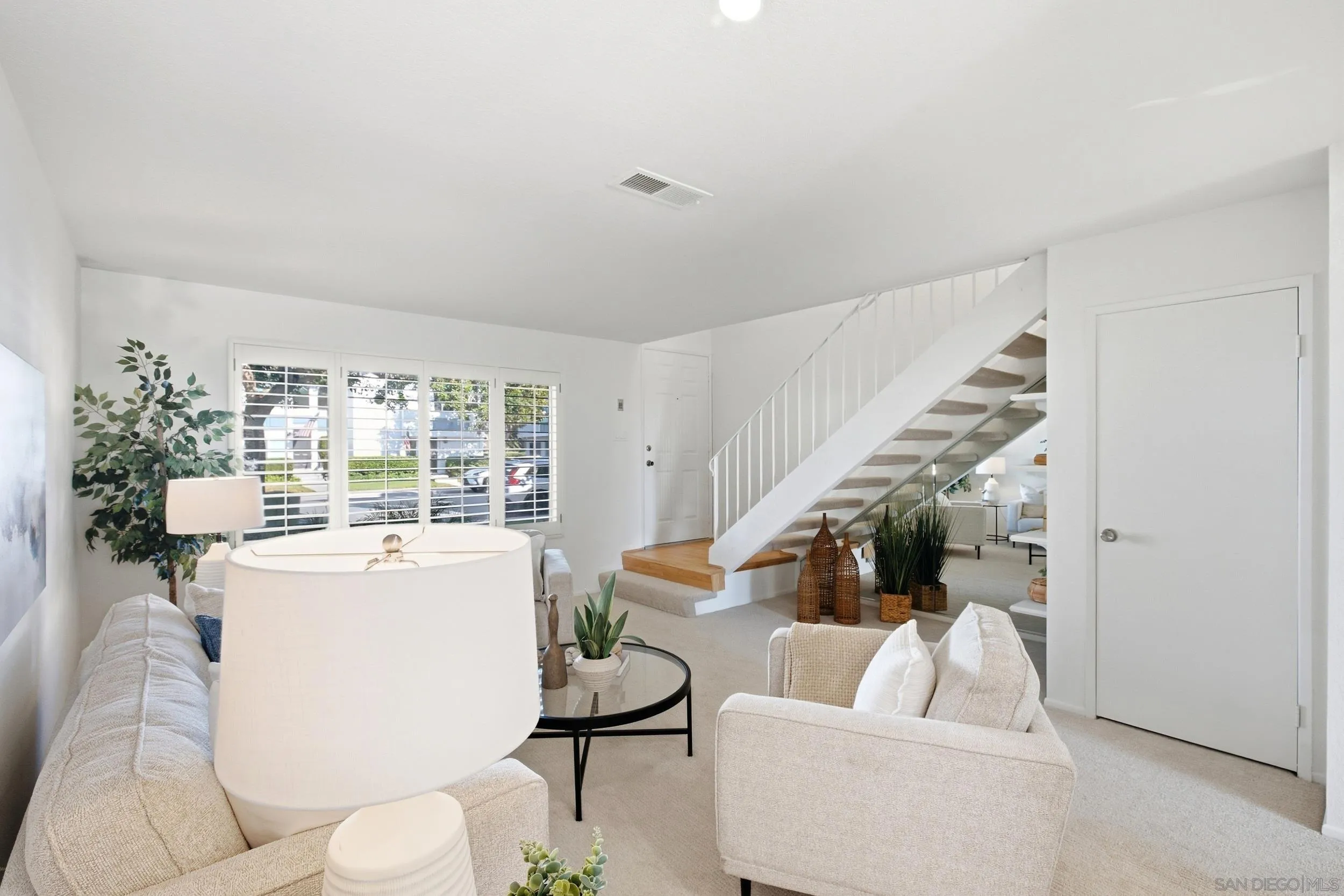 Bright living room with white sofas, shuttered windows, and a staircase with wood treads.