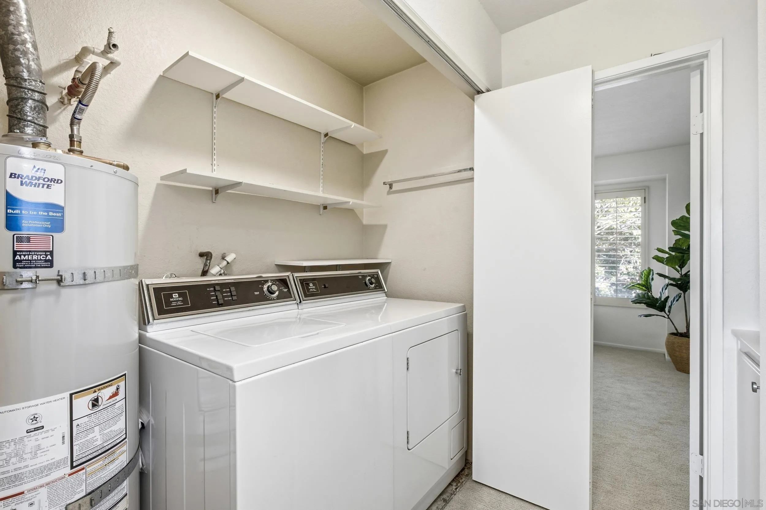 Laundry room with washer, dryer, water heater, and open wall shelves.