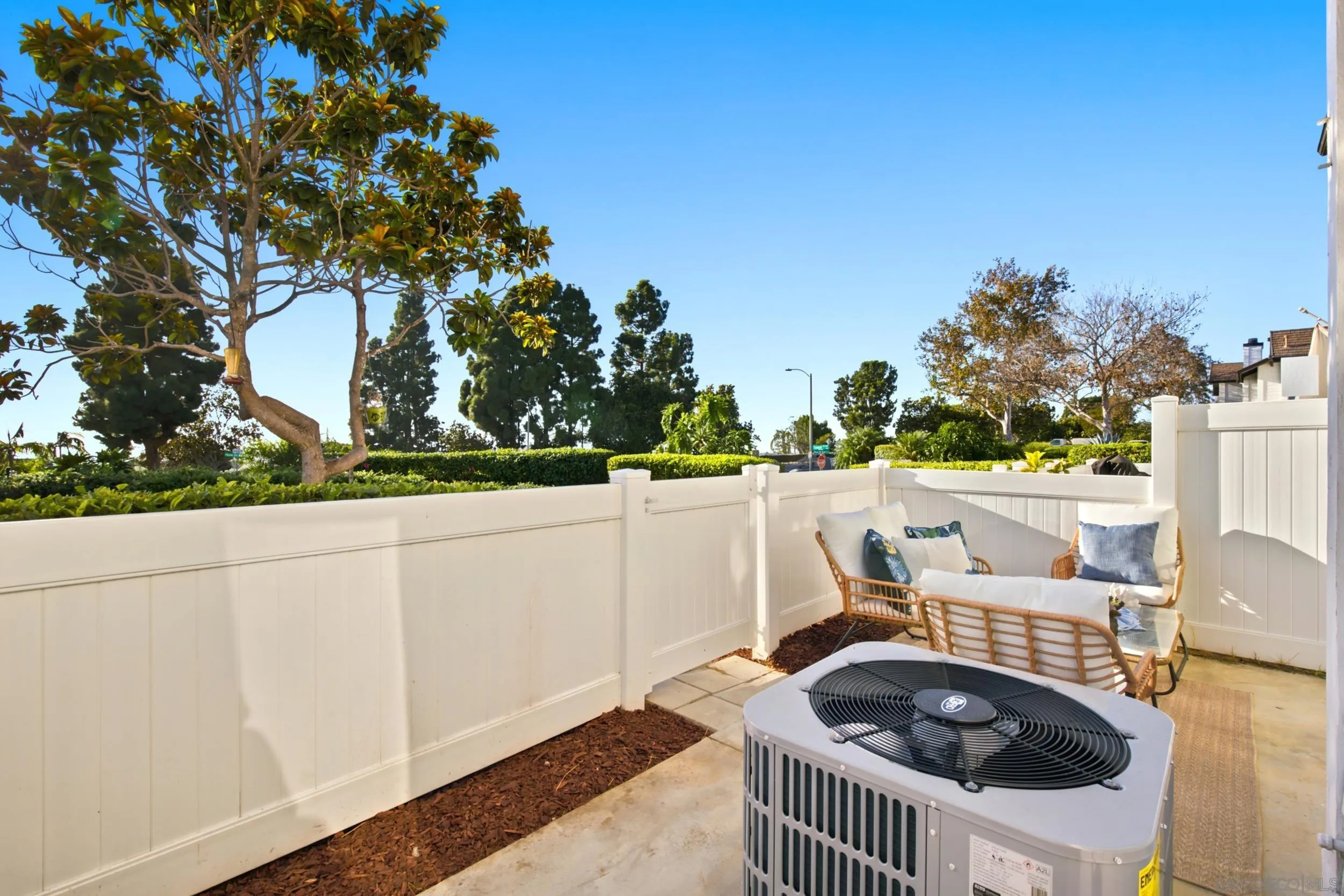 Fenced patio with wicker seating and an air-conditioning condenser in the foreground.