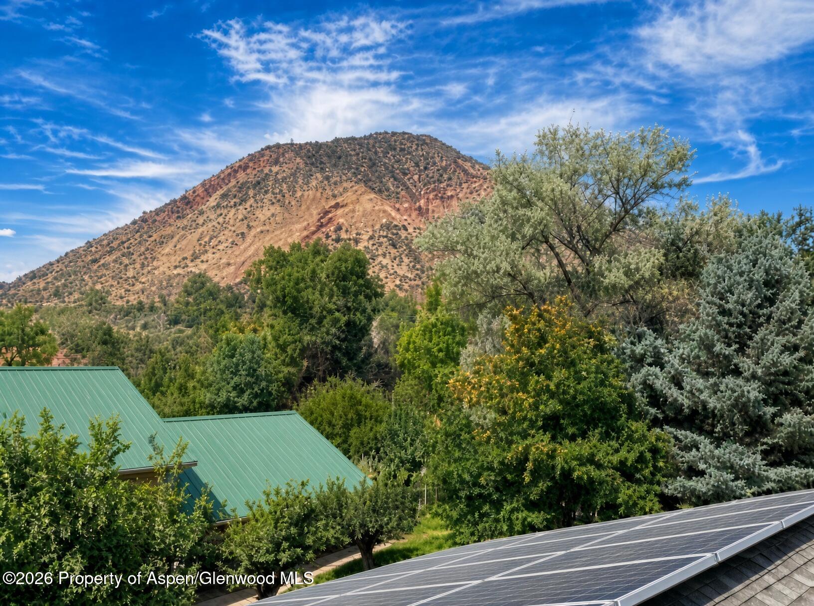 Mountain view above leafy trees, with green metal roofs and solar panels in the foreground.